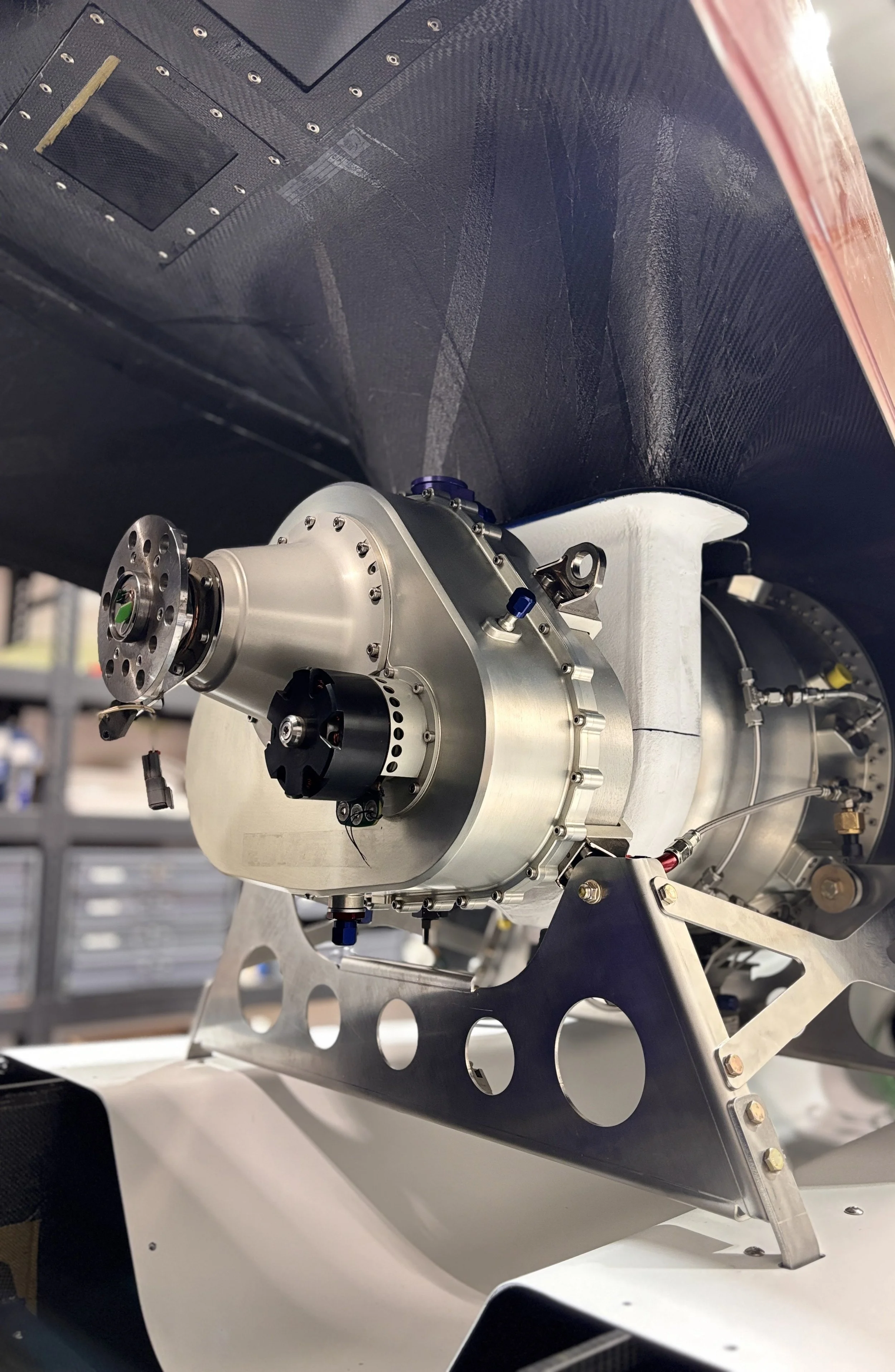 Close-up of a high-precision spacecraft engine or thruster mounted on a metallic framework inside a space laboratory or manufacturing facility.