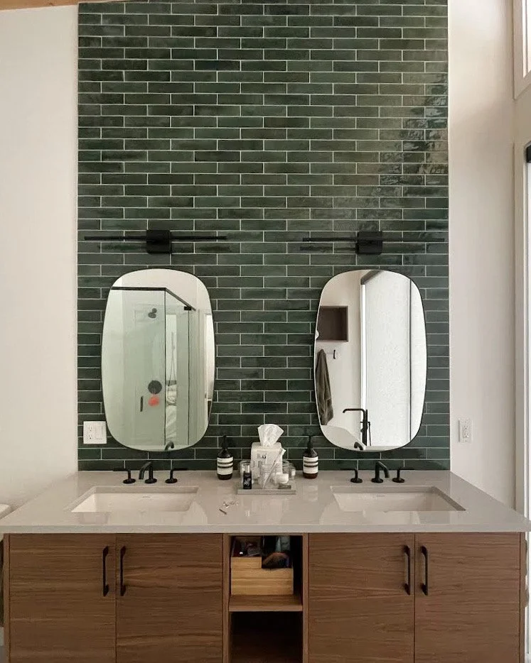 A modern bathroom vanity with two oval mirrors, black fixtures, and a wooden cabinet with a white countertop.