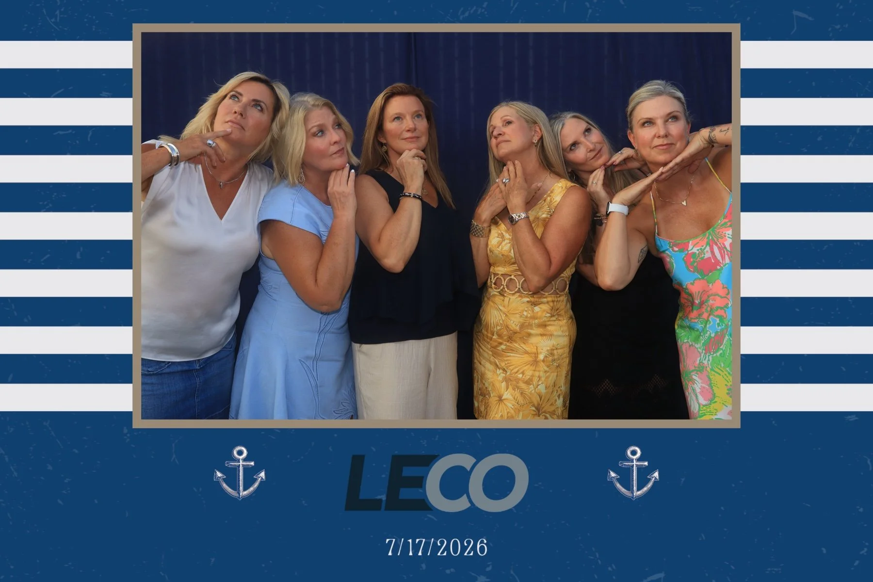 Group of six women standing together in front of a blue curtain, posing thoughtfully with their hands near their chins or cheeks, for a photo at a Leo-themed event on July 17, 2026.