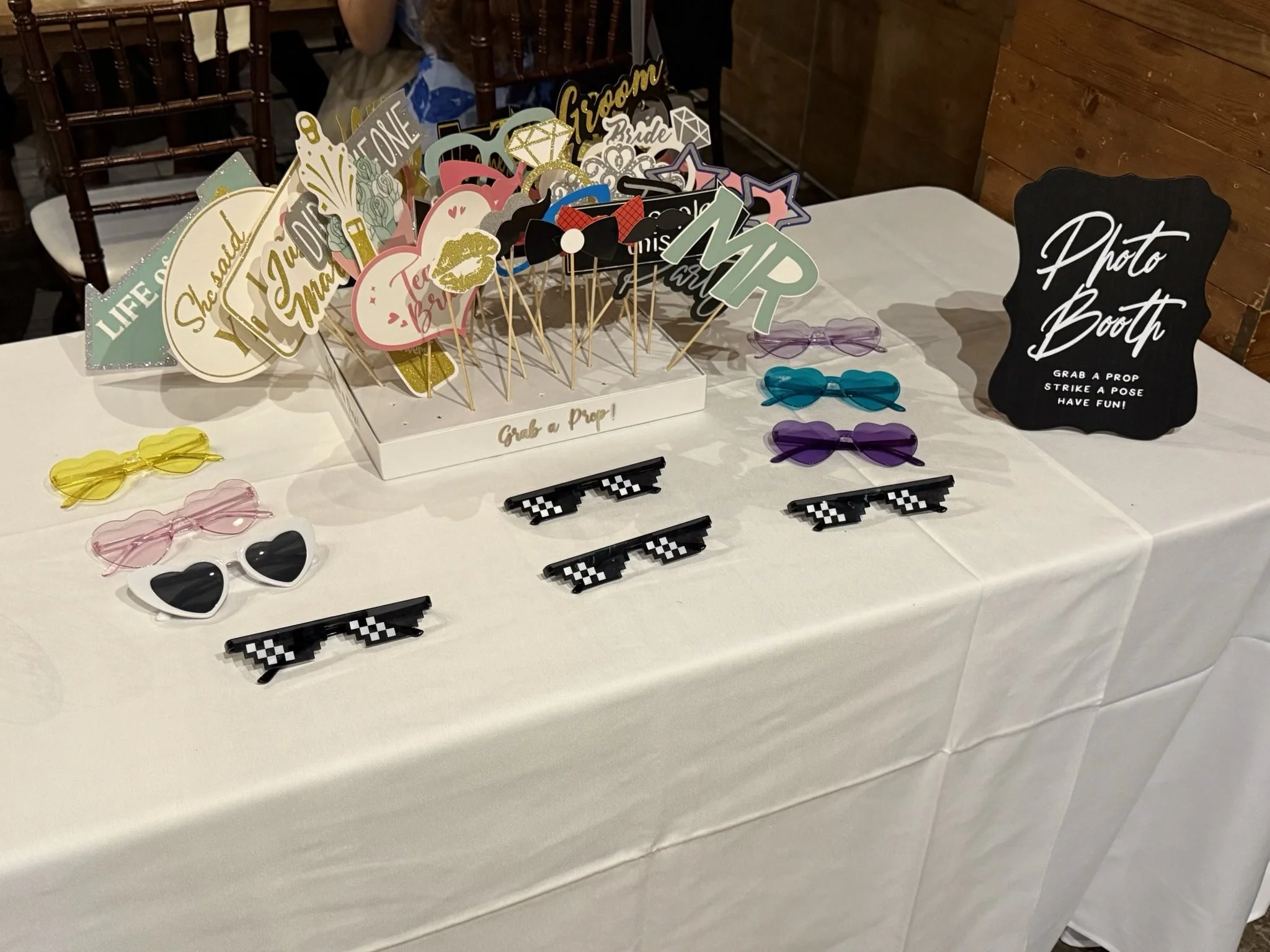 Table with photo booth props including sunglasses, signs, and various cutouts, with a black sign reading 'Photo Booth.'