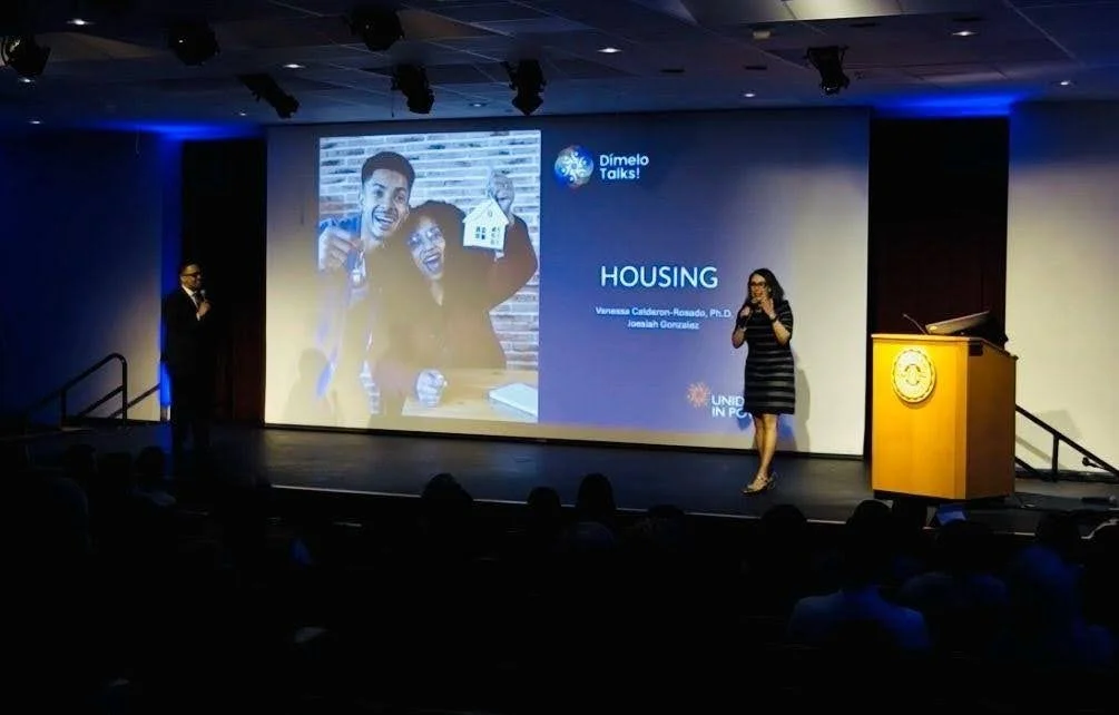 Presentation on housing with two speakers on stage and a large screen displaying a happy family holding a house key.