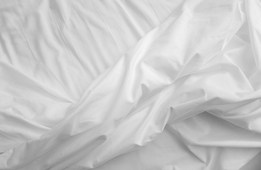 Close-up of smooth, white, crumpled fabric or bedsheet.