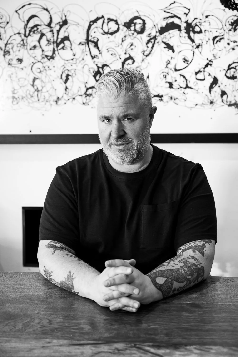 Matt Thomas seated at a wooden table beneath abstract artwork