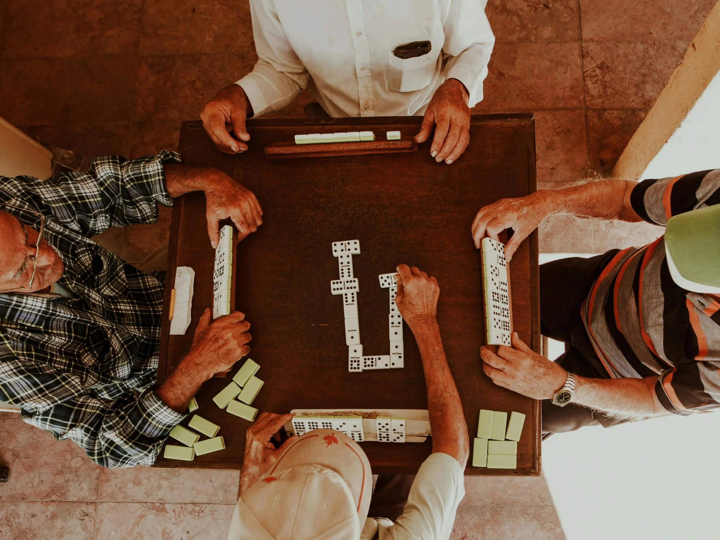 A group of adults sitting around a table playing dominoes together, sharing a moment of connection.