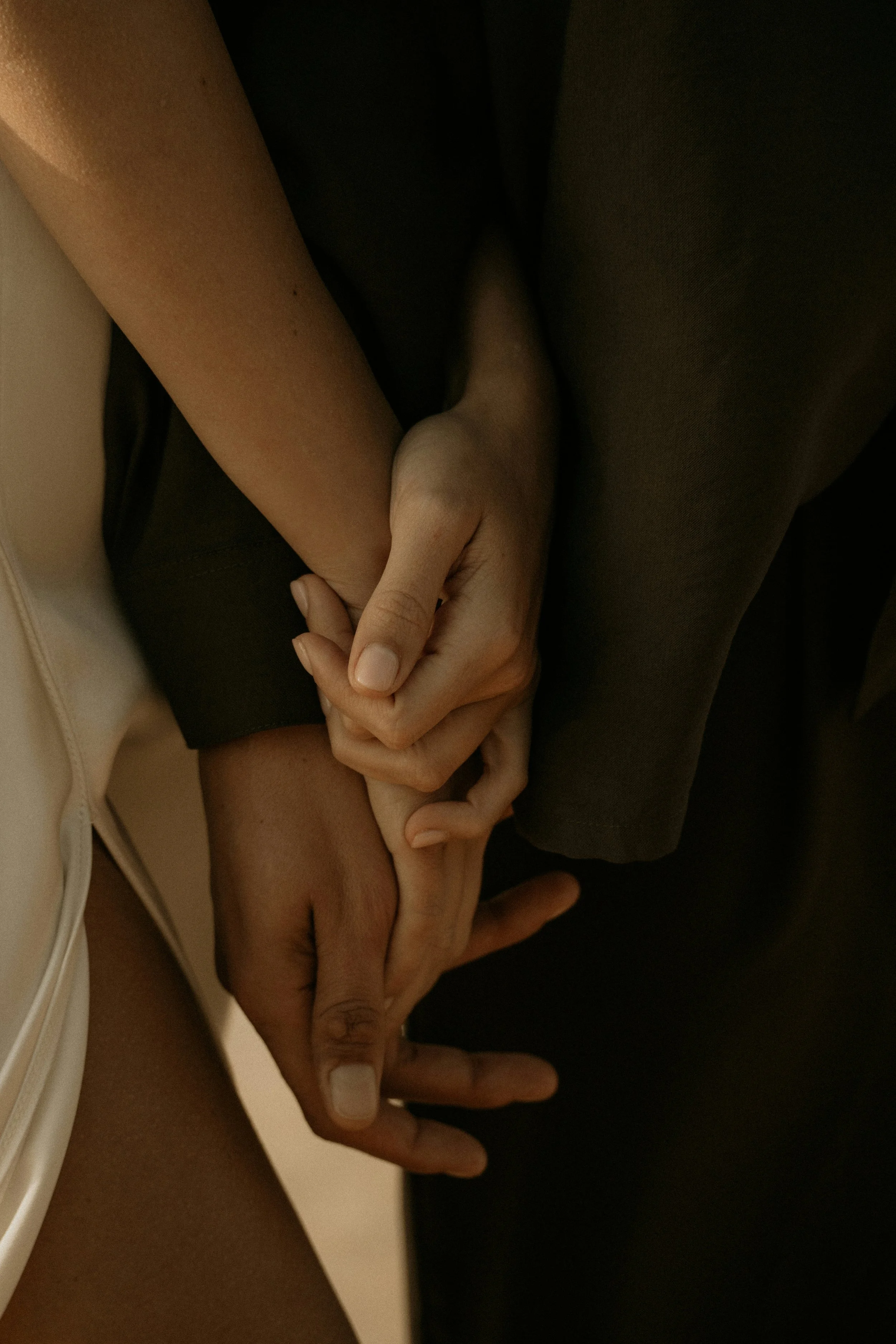 A close-up of a couple holding hands in a warm light.