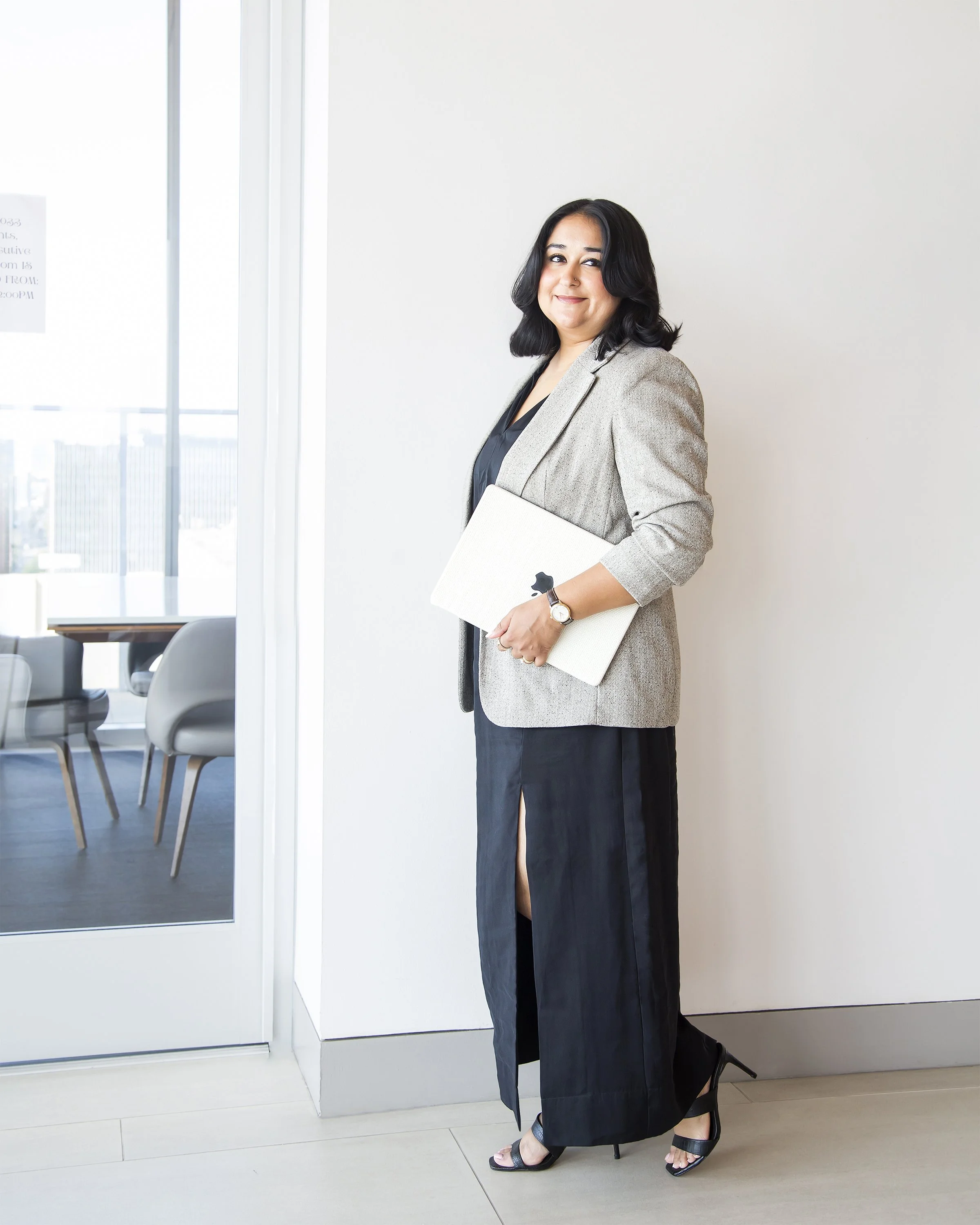 Corporate portrait of a South East Asian Indian woman walking into a conference room holding her laptop.