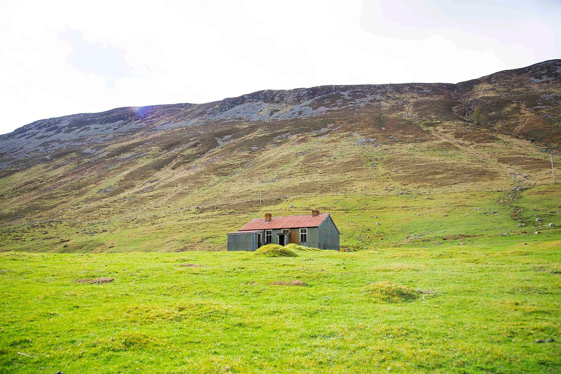 Photograph of an abandoned house in the green hills of a glen in Scotland.
