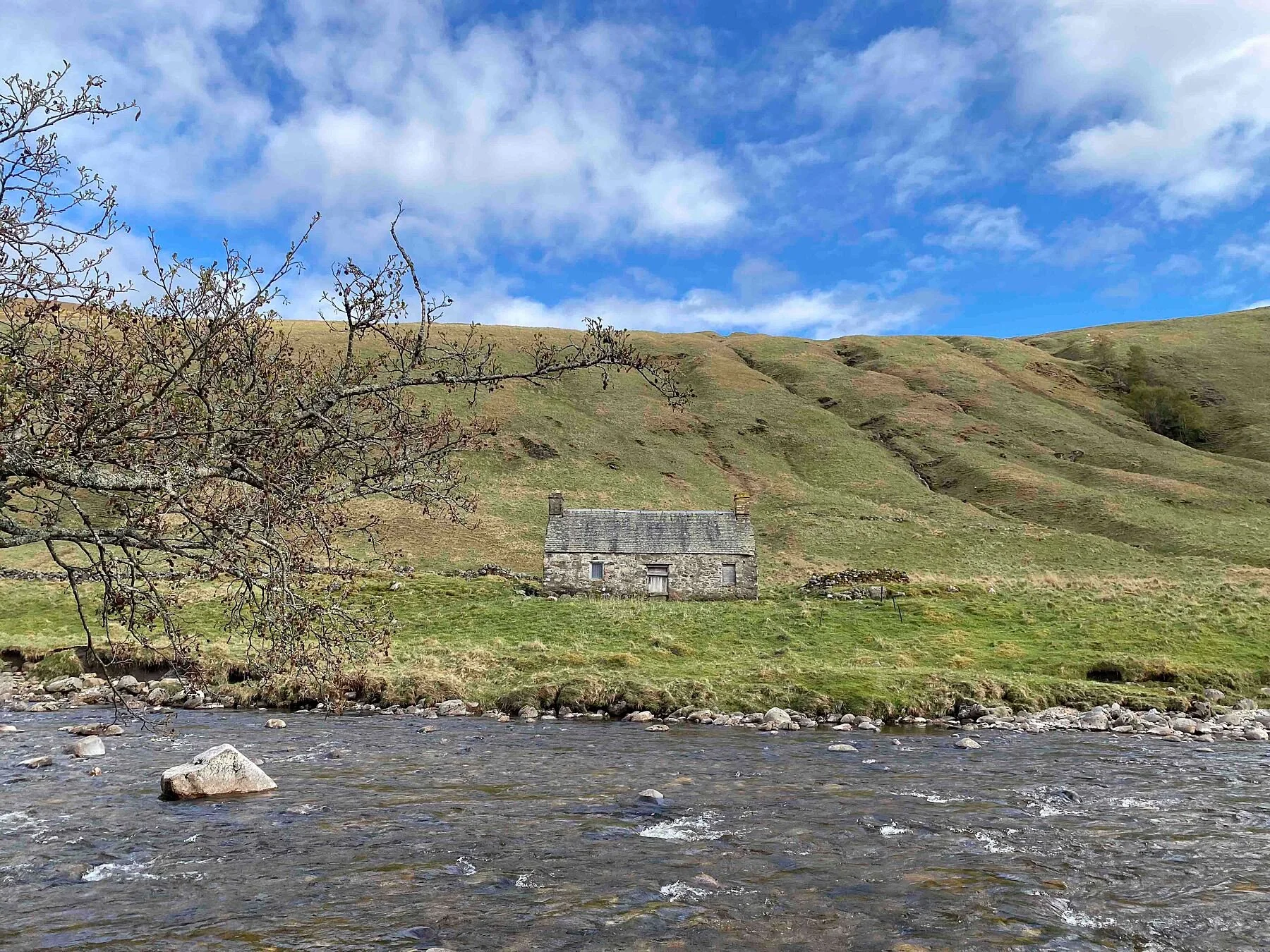 Photograph of a stone cottage under a bright blue sky on the bank of the River Tilt in Scotland.
