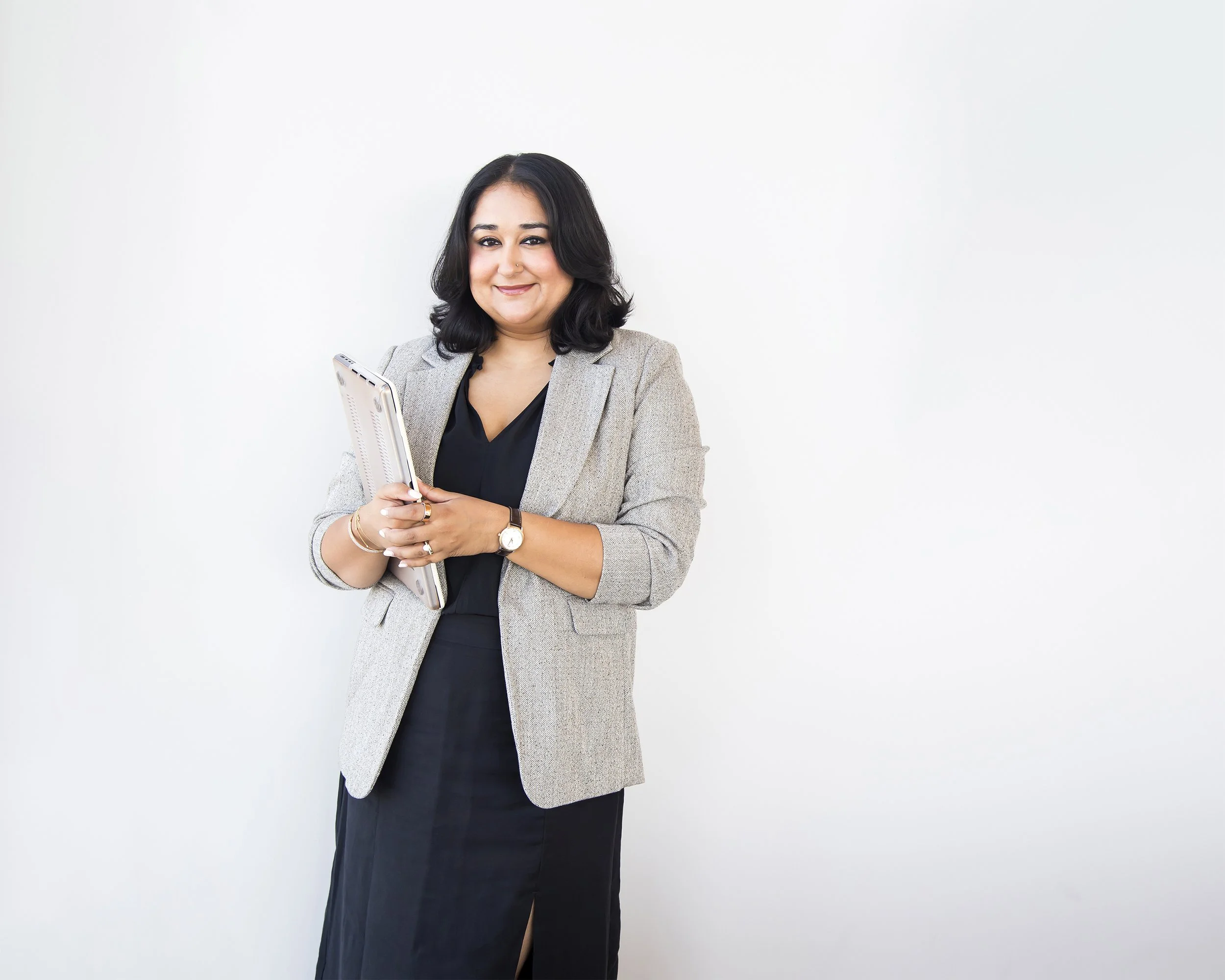 Corporate portrait of a marketing CEO holding her laptop against a white wall. 