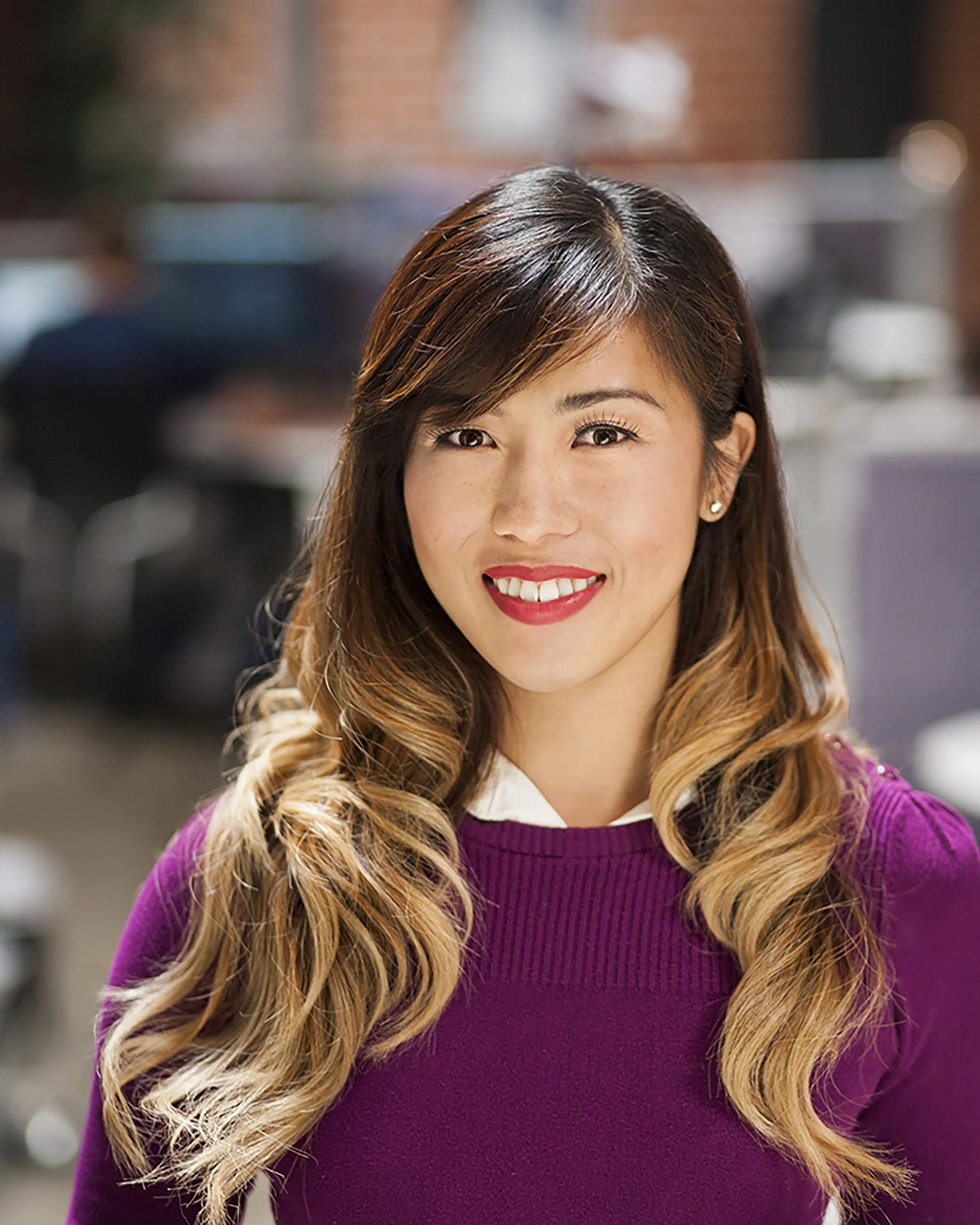 Portrait of an Asian American woman wearing a purple sweater in an office setting.