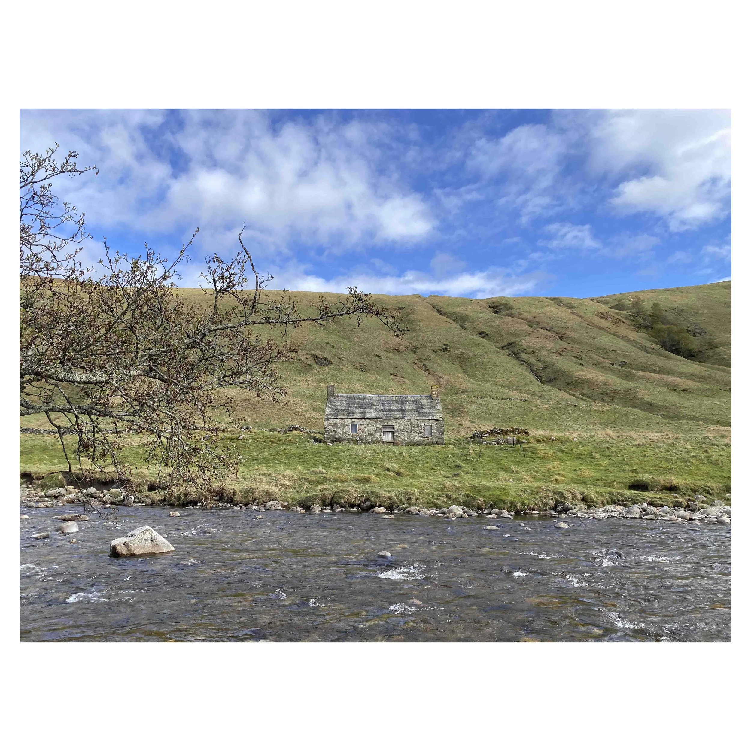 Photograph of a stone cottage under a bright blue sky on the bank of the River Tilt in Scotland.