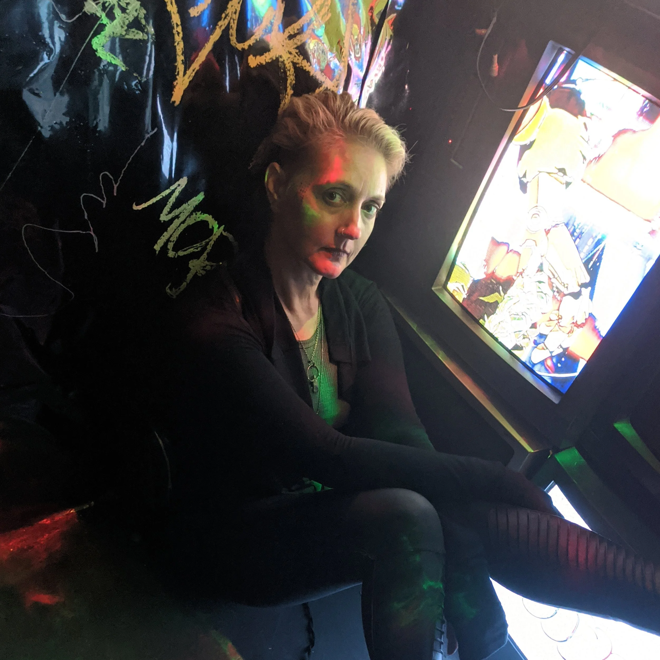 Image of Lauren Elisabeth sitting in a cyberpunk style photoshoot set with neon lighting surrounding her.