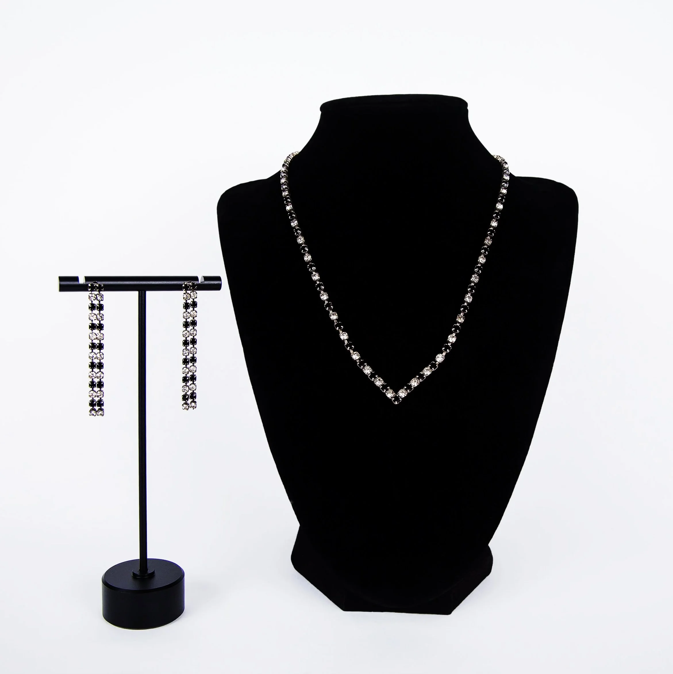 A black and white rhinestone jewelry set of earrings and necklace. The set is in the 1940s art deco style. It is displayed on jewelry stands on a white background.