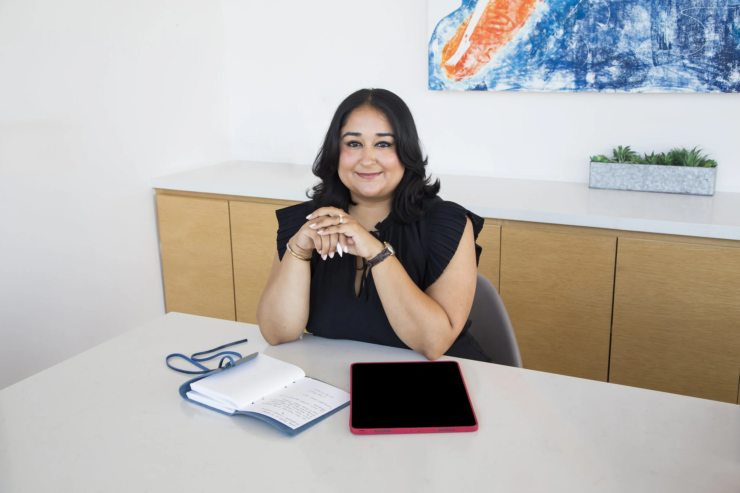 A South East Asian Indian woman sits at a conference table with her planner and an iPad in front of her. 