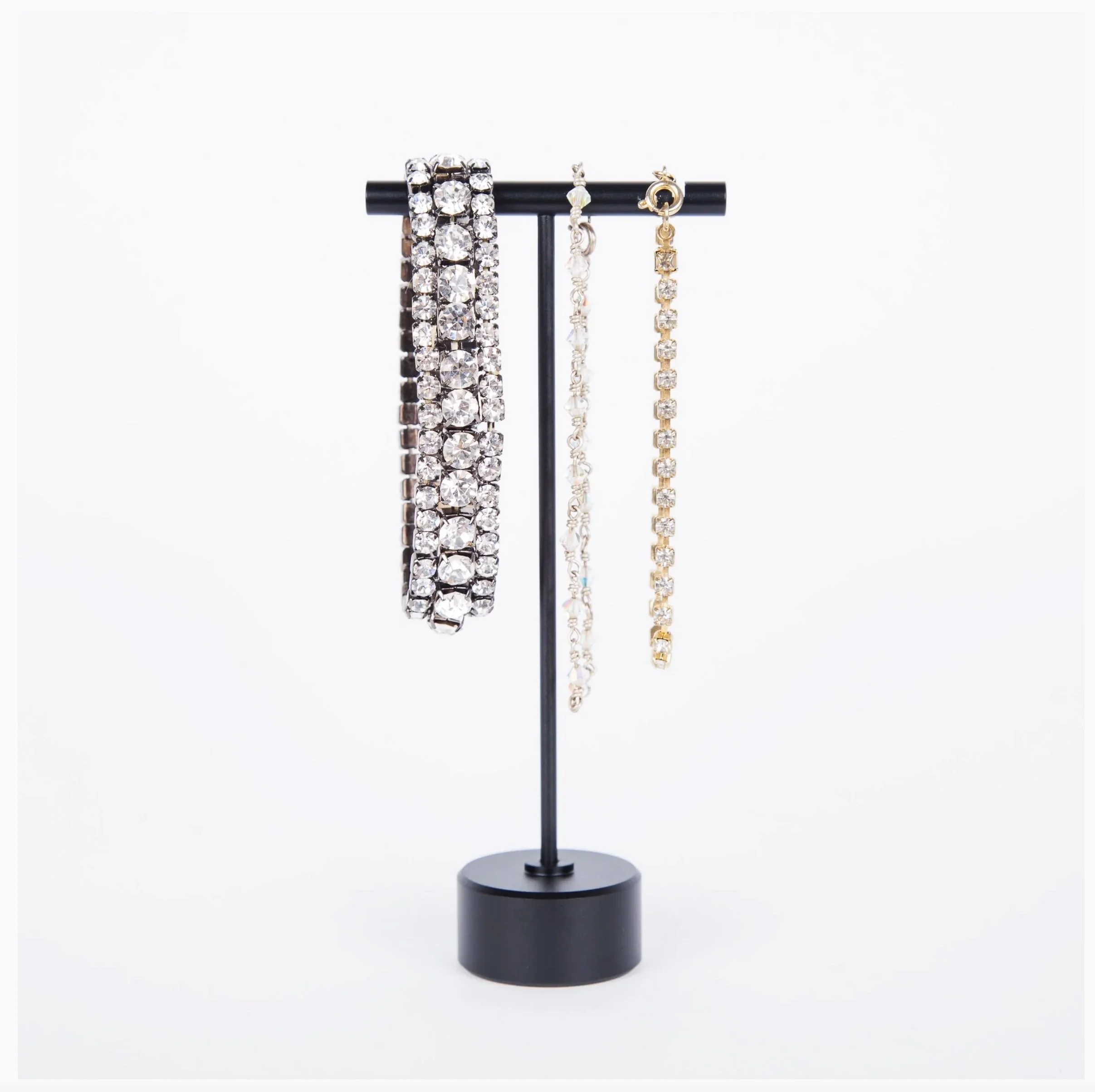 A set of three rhinestone tennis bracelets displayed on a hanging jewelry rack. The bracelets include a stretch rhinestone bangle, a beaded tennis bracelet and a rhinestone tennis bracelet. 