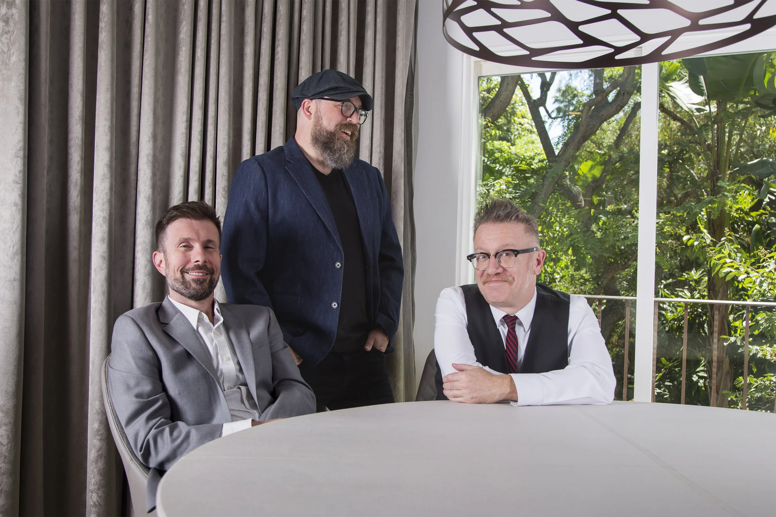 Three men around a conference table with a large window behind them. They are laughing.