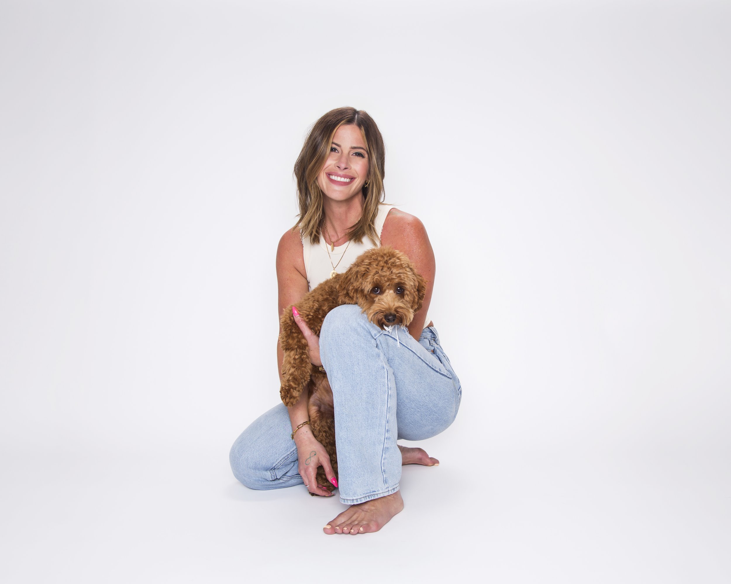 Portrait of a blonde woman and her golden doodle puppy posing on a white background.