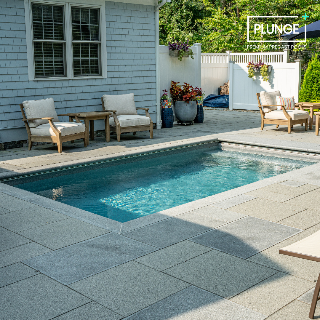 A backyard with a small swimming pool, outdoor lounge chairs, potted plants, and a white privacy fence.