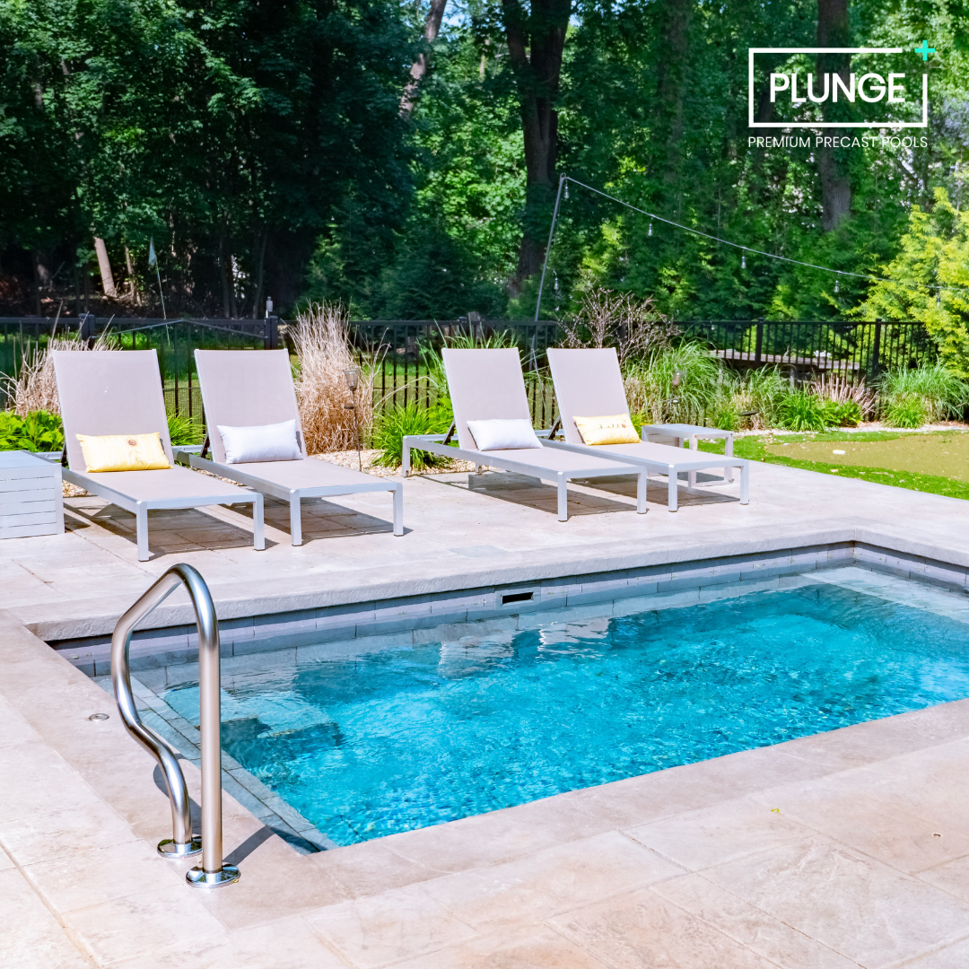 A backyard with a rectangular swimming pool, three lounge chairs with pillows, and lush green trees in the background, with a logo that says "PLUNGE PREMIUM PRECAST POOLS."