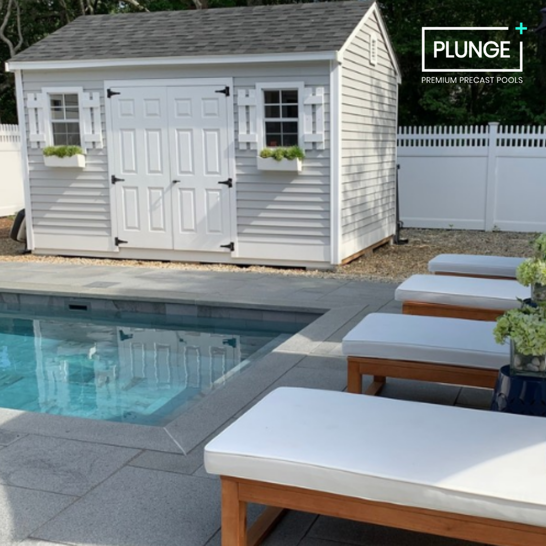 A backyard pool area with lounge chairs and a white storage shed with windows and shutters.