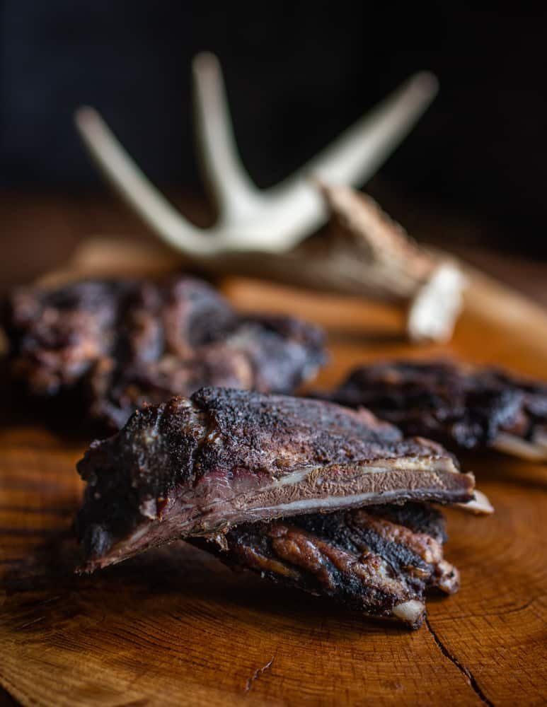Close-up of cooked beef ribs on a wooden cutting board with a piece of antler in the background.
