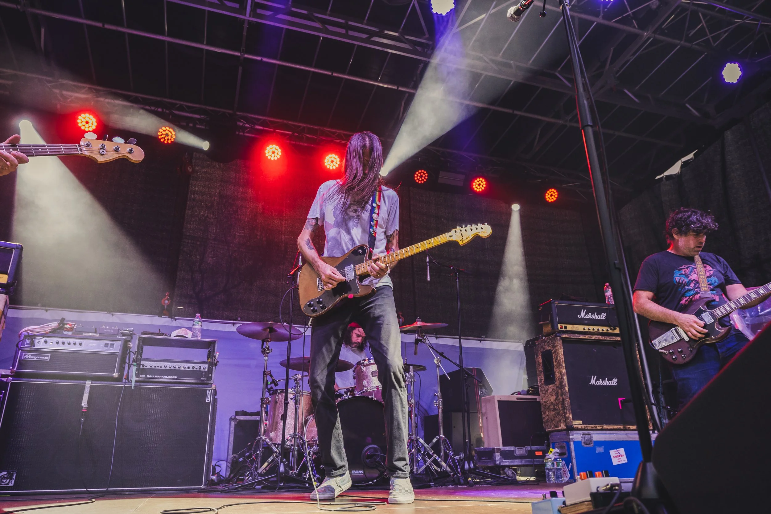 Band performing on stage with guitars and drums, stage lighting with red and yellow lights.
