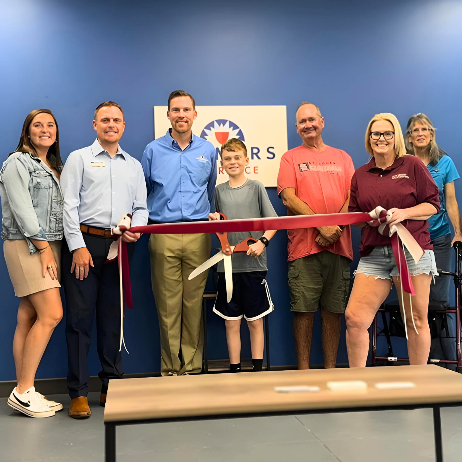 Group of people at ribbon-cutting ceremony in front of a blue wall with a logo.