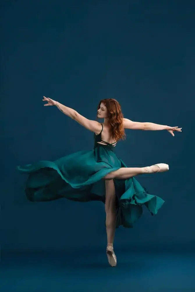 Ballet dancer in a green dress performing a pose on pointe against a dark blue background.