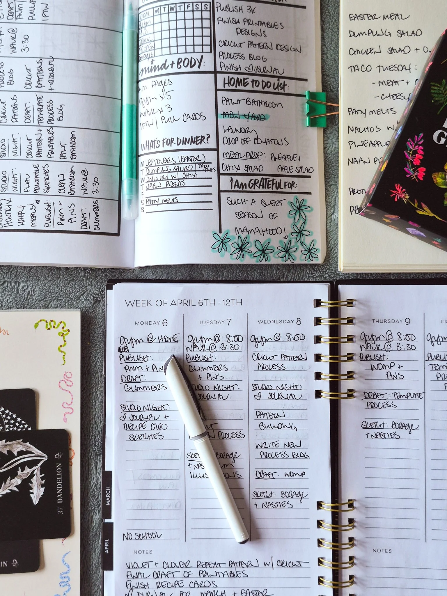 a cozy creative planning routine showing two open planners and two notepads filled with creative plans, weekly meal plans and oracle notes to remember