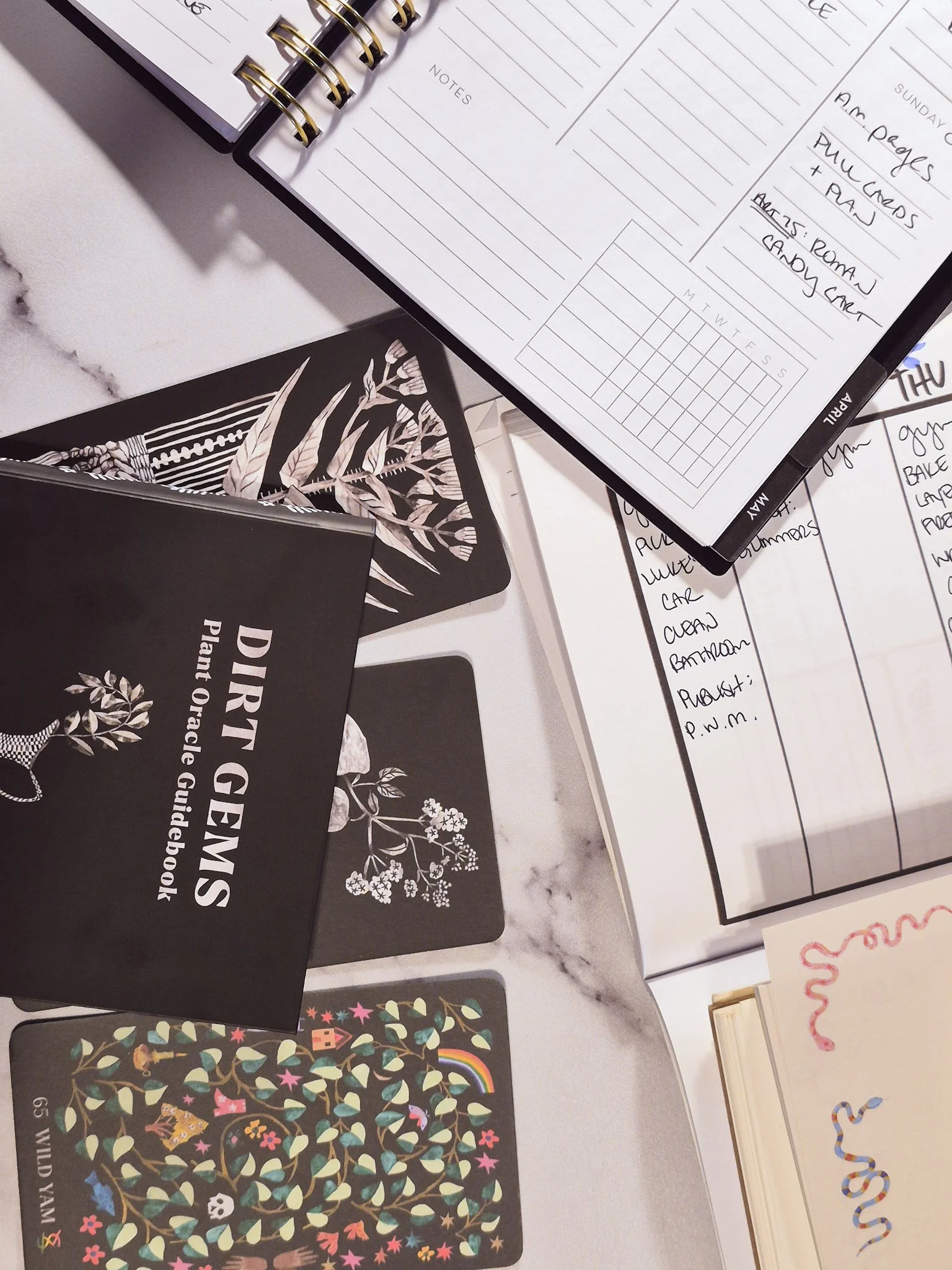 closeup of planning set up with weekly and monthly planners and a set of oracle cards nearby set against a marble background