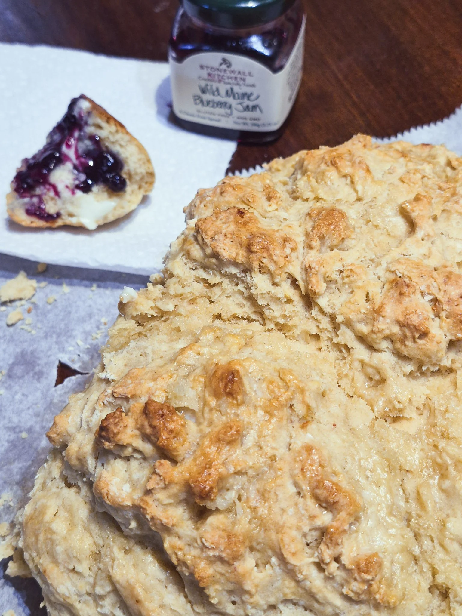 close up of a loaf of irish soda bread with a chunk broken off, slathered in butter and jam