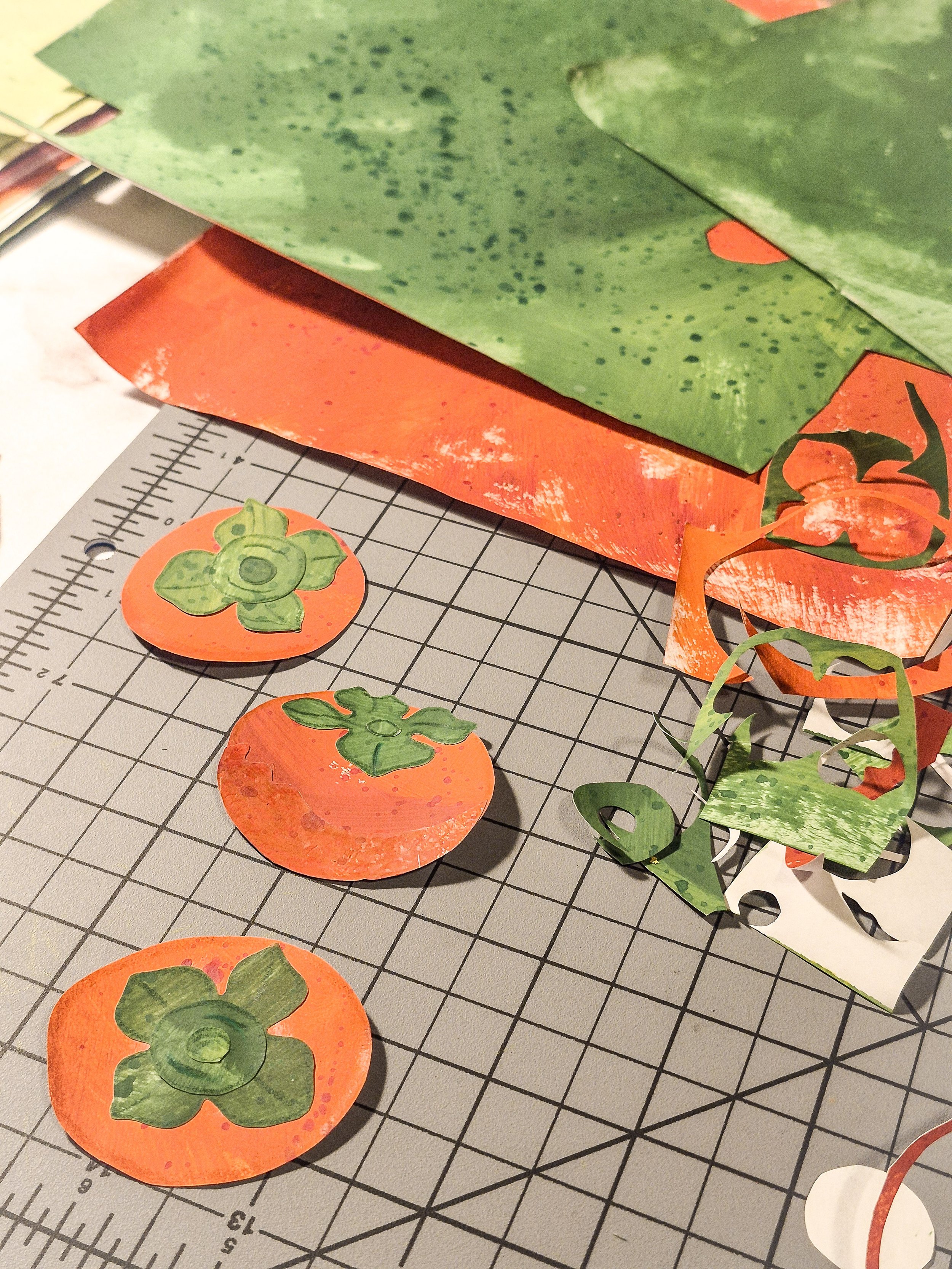 Hand-cut painted paper persimmon motifs with green leaves and cut paper scraps