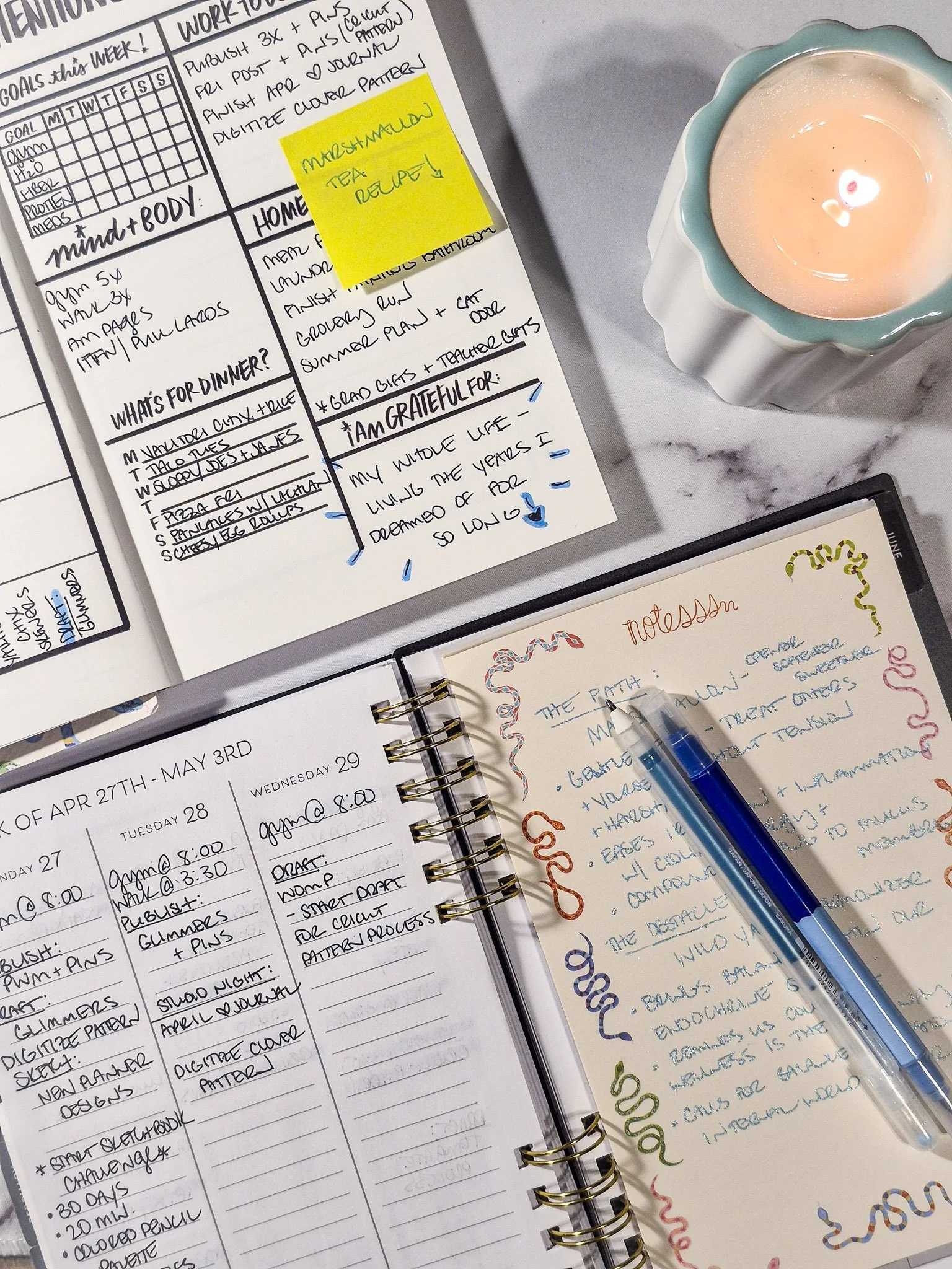Weekly planner page featuring a gratitude section, yellow sticky note reminder, and lit candle for a cozy planning moment