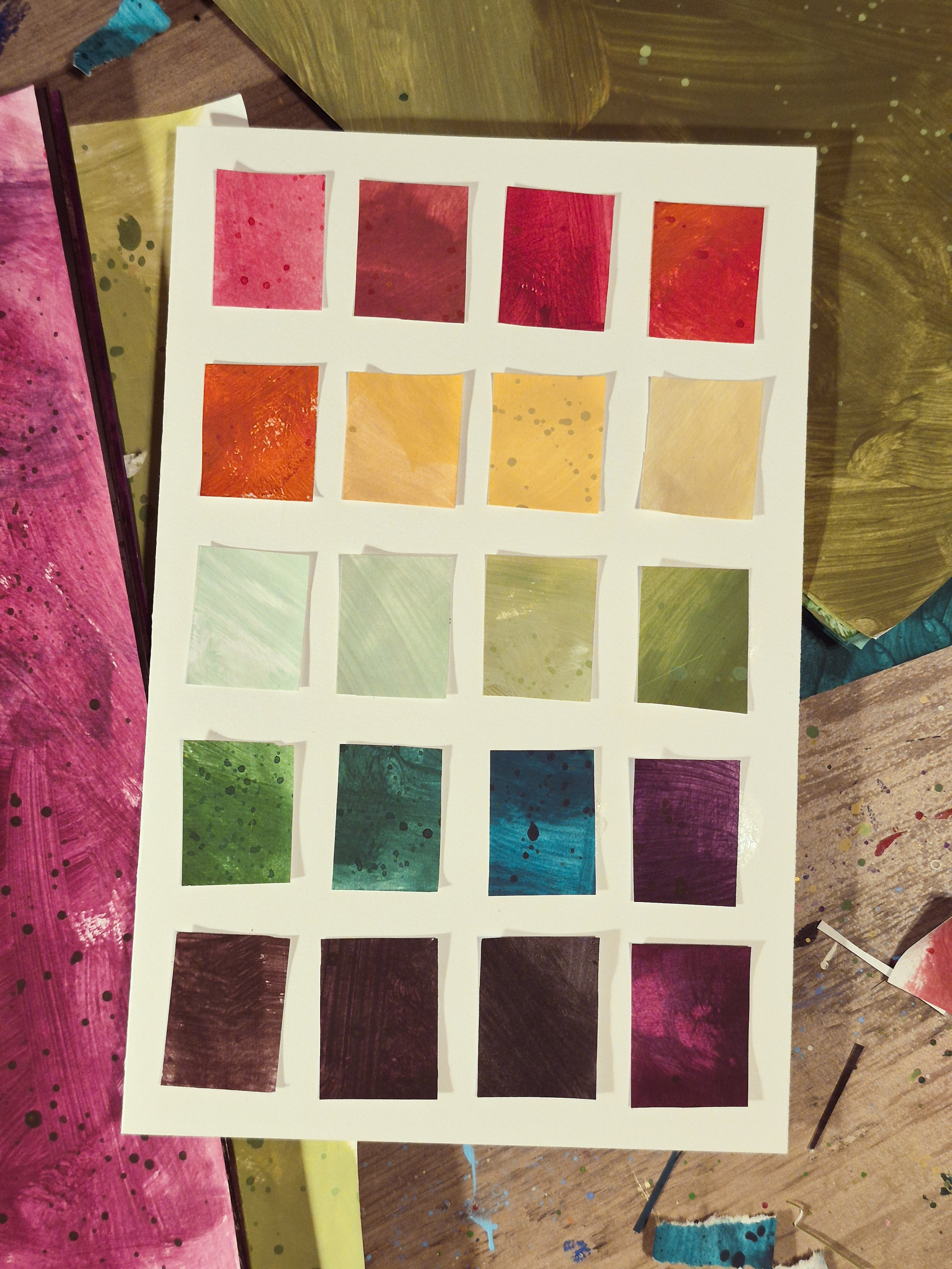 Grid of handmade painted-paper color swatches in pink, red, orange, yellow, green, teal, blue, purple, and brown tones arranged on a white sheet.