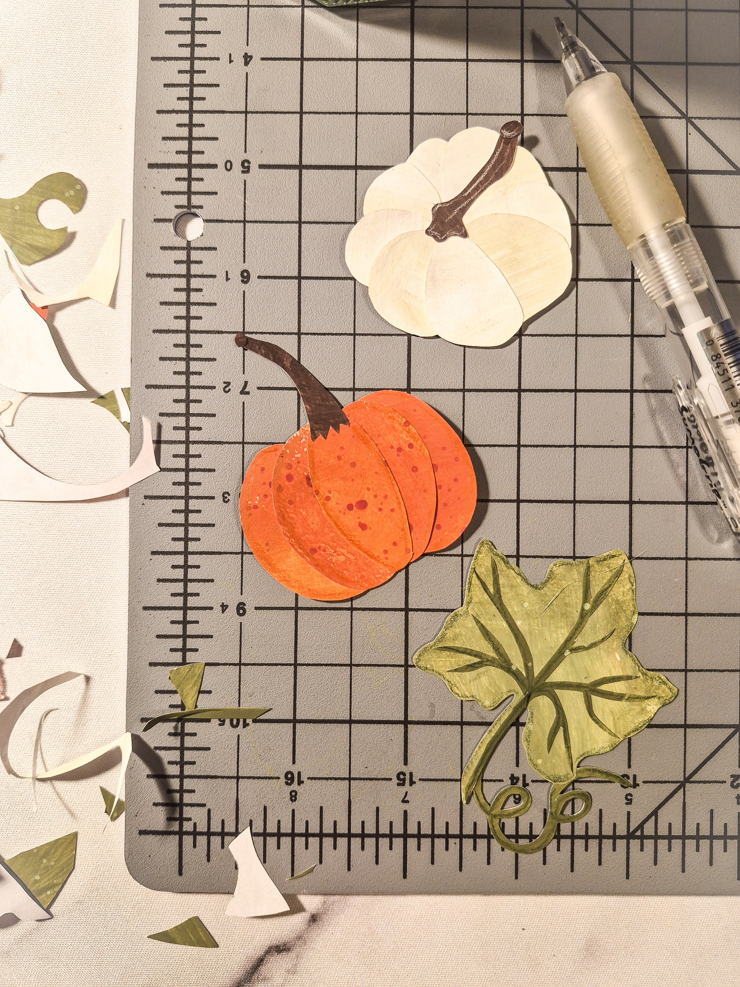 Close-up of a painted paper pumpkin, pale pumpkin, and leafy vine motif on a cutting mat