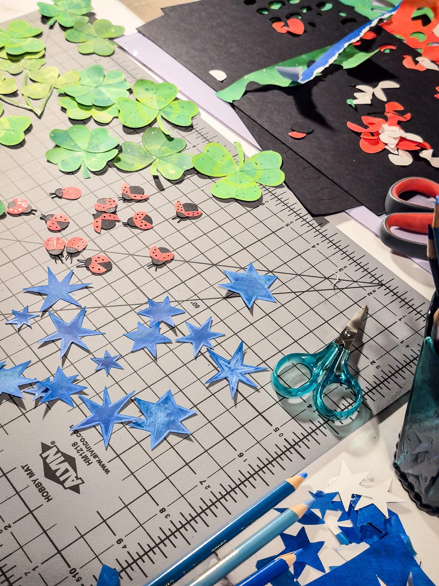 Full workspace view showing cut paper collage elements, tools, and materials used to create an analog repeat pattern