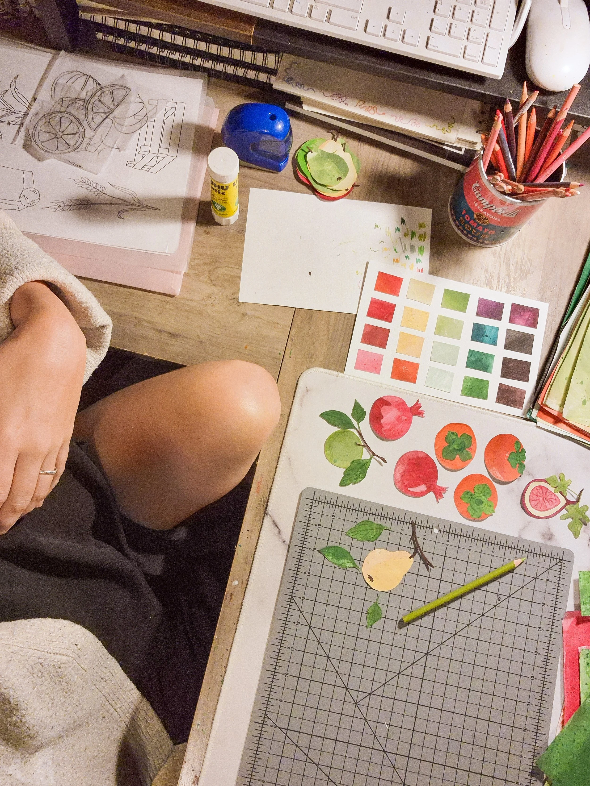 Painted paper persimmons, pomegranates, pears, and leaves arranged on a studio worktable