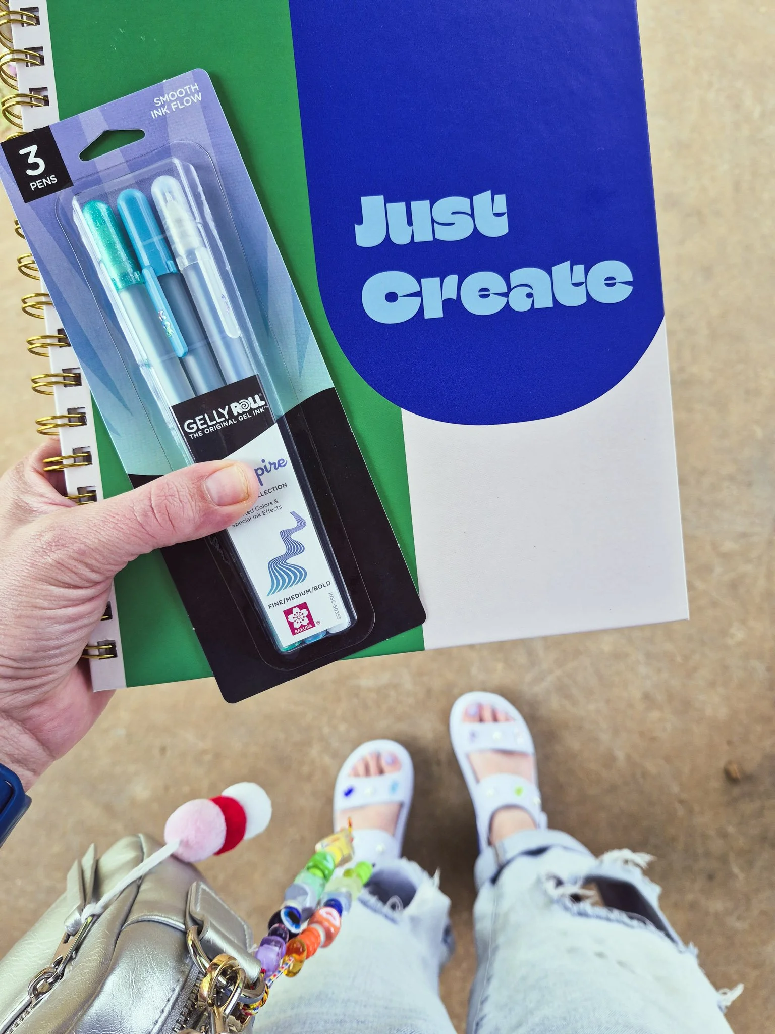 Hand holding gel pens and a notebook that says “Just Create” during a trip to the craft store