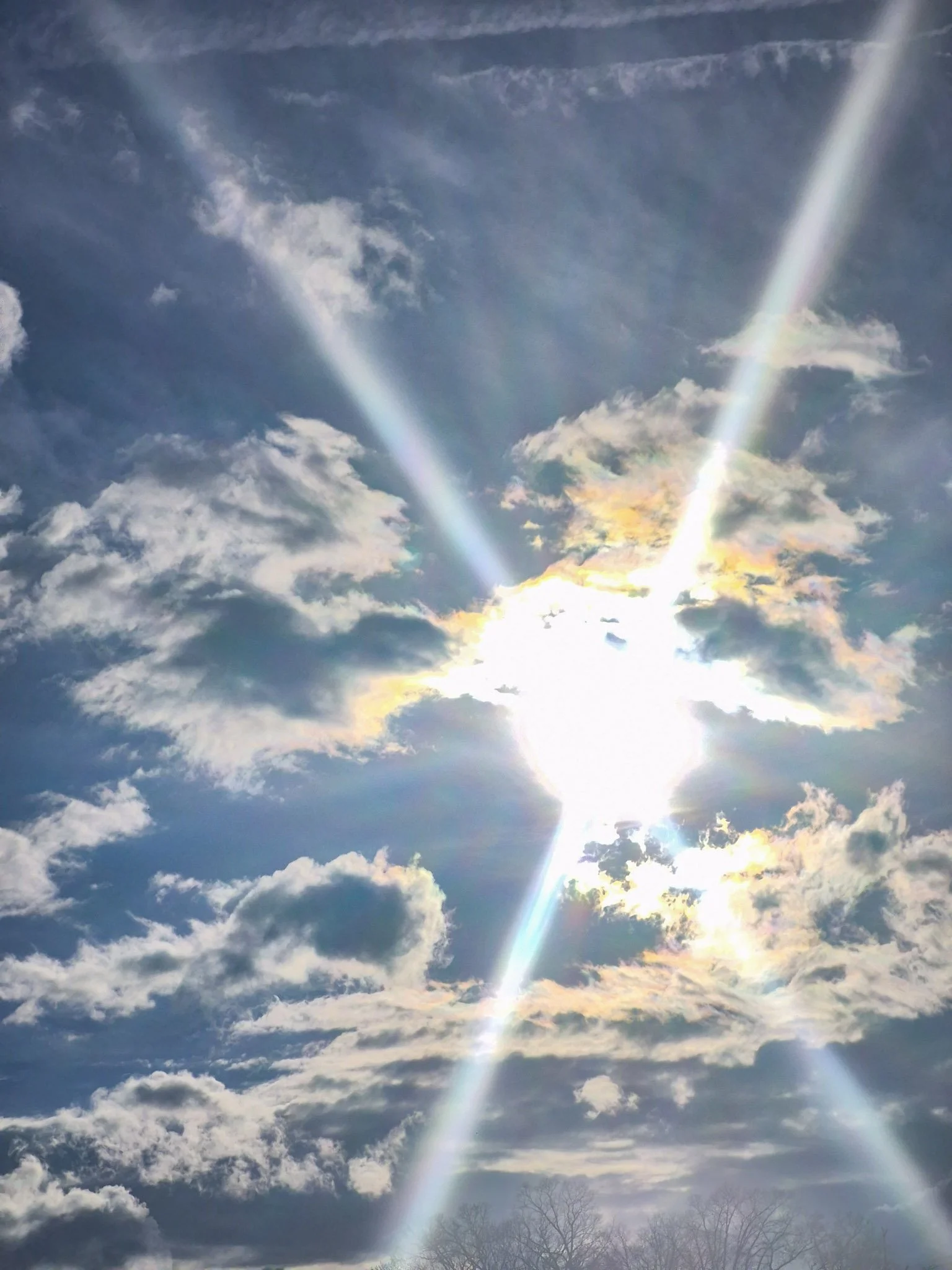 image of a partly cloudy sky with the bright sun causing a rainbow lens flare