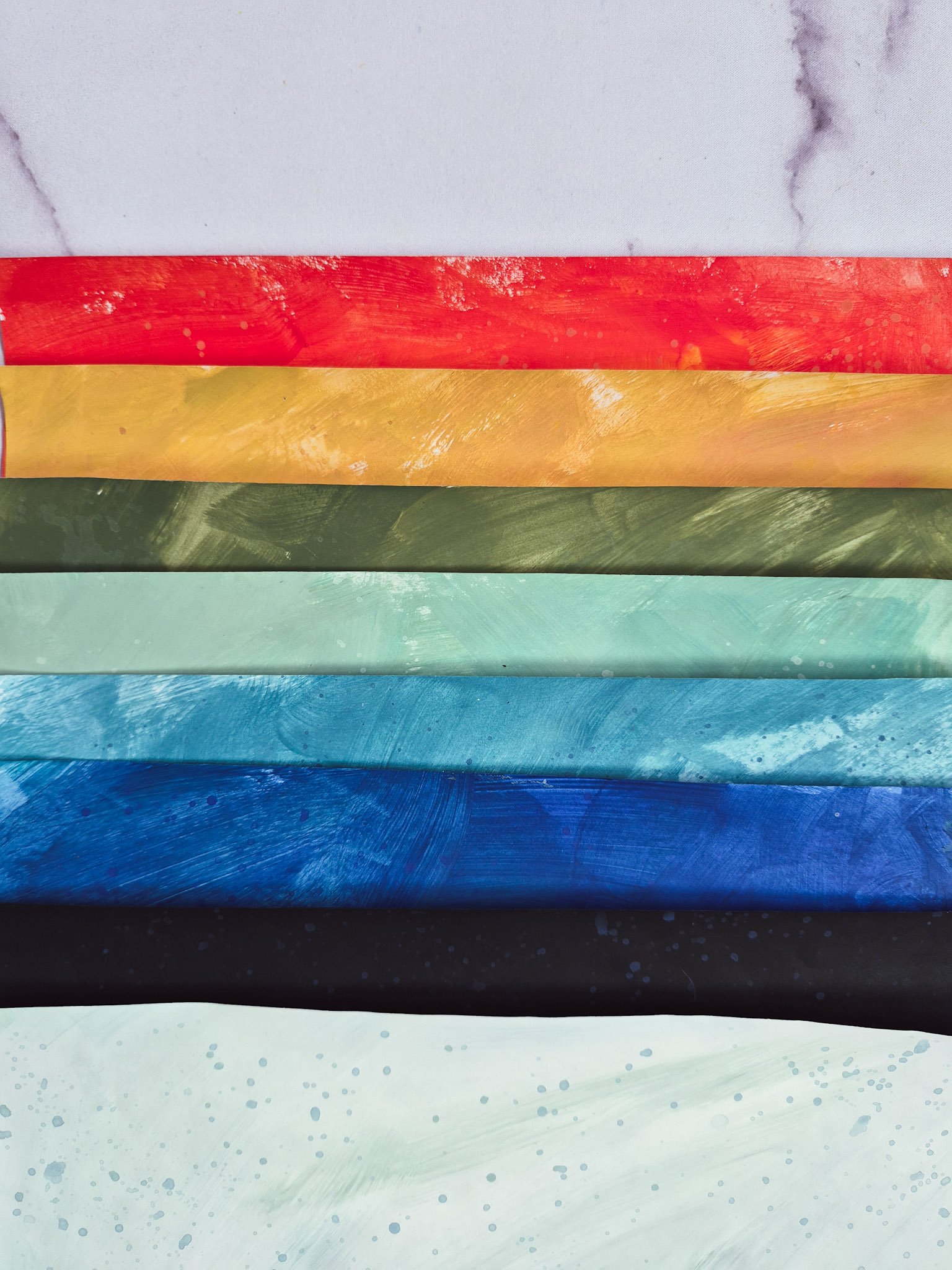flat lay of hand-painted collage papers arranged in a gradient on marble background