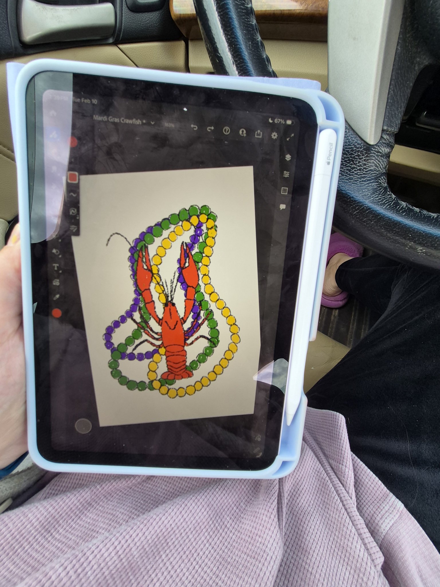 overhead shot of artists lap with ipad open to a digital illustration of crawfish with mardi gras beads in background