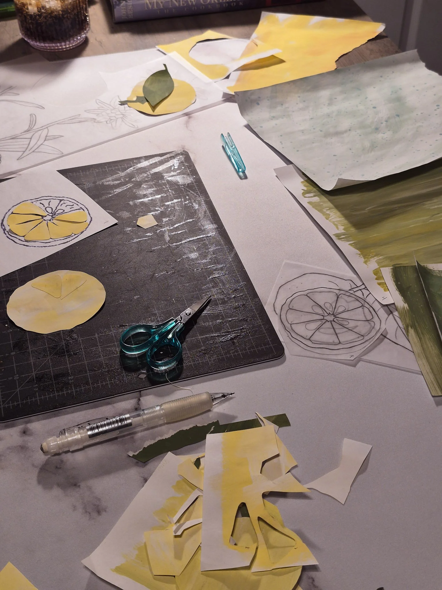 desk shot of papercut collage process with handmade papers and templates and scissors strewn across the desk