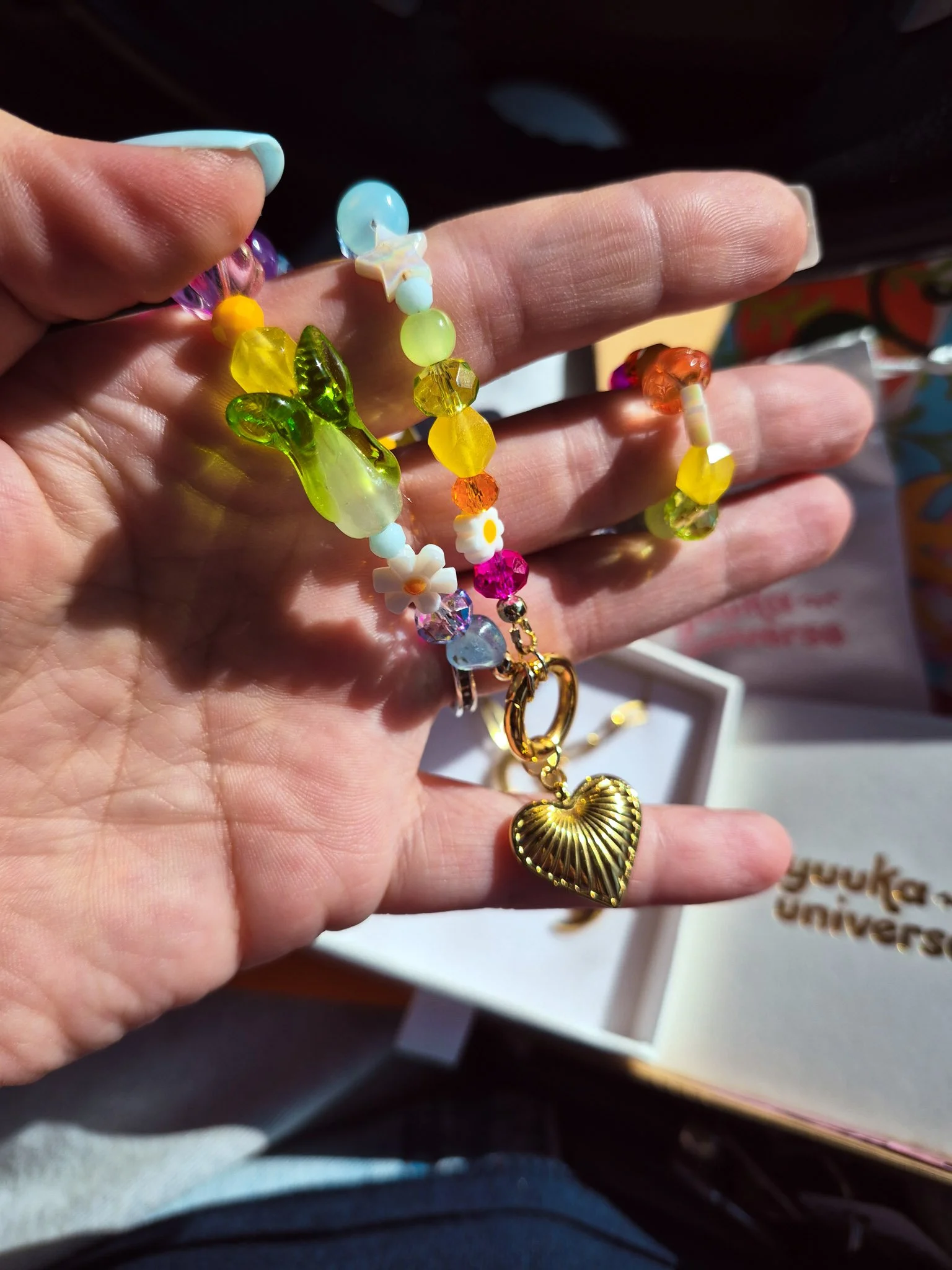 Close-up of a hand holding a colorful handmade beaded charm bracelet with translucent beads and a gold heart pendant.