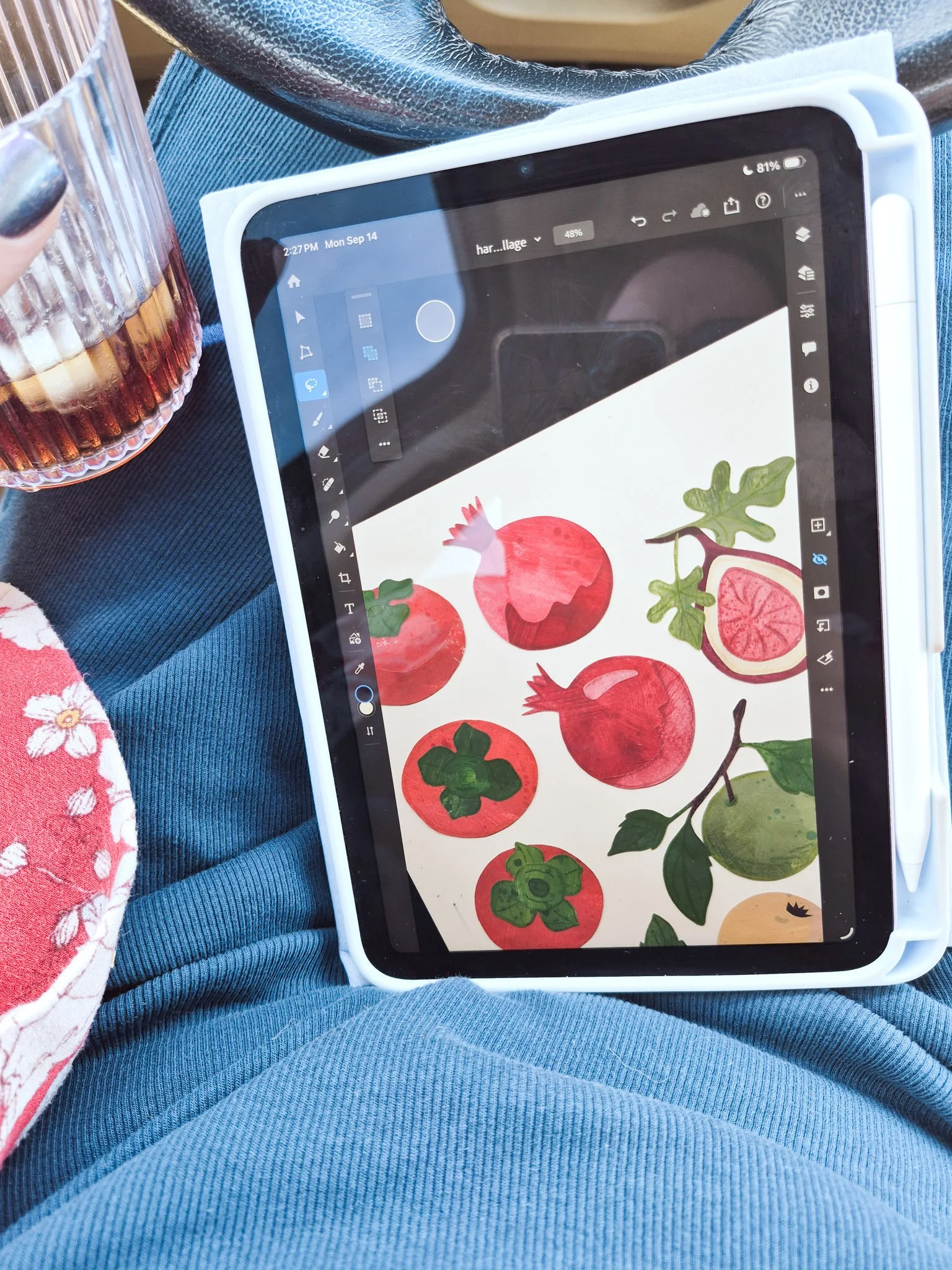 An iPad displaying painted paper collage artwork of persimmons, pomegranate, leaves, and other autumn fruits.