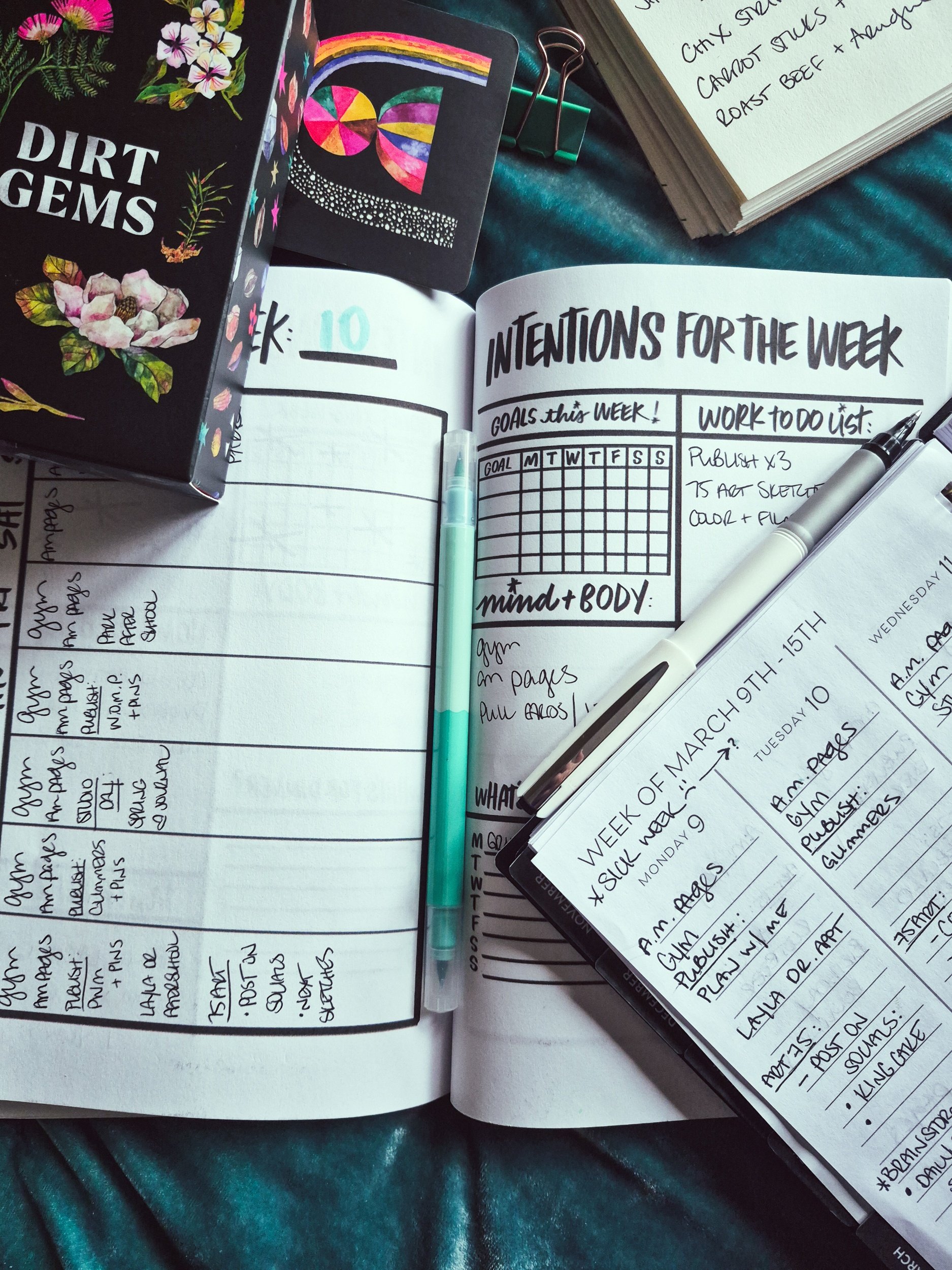 creative planning layout with an open intentions for the week planner, notepad, and an oracle card from the Dirt Gems deck all laying atop a teal velvet bedspread