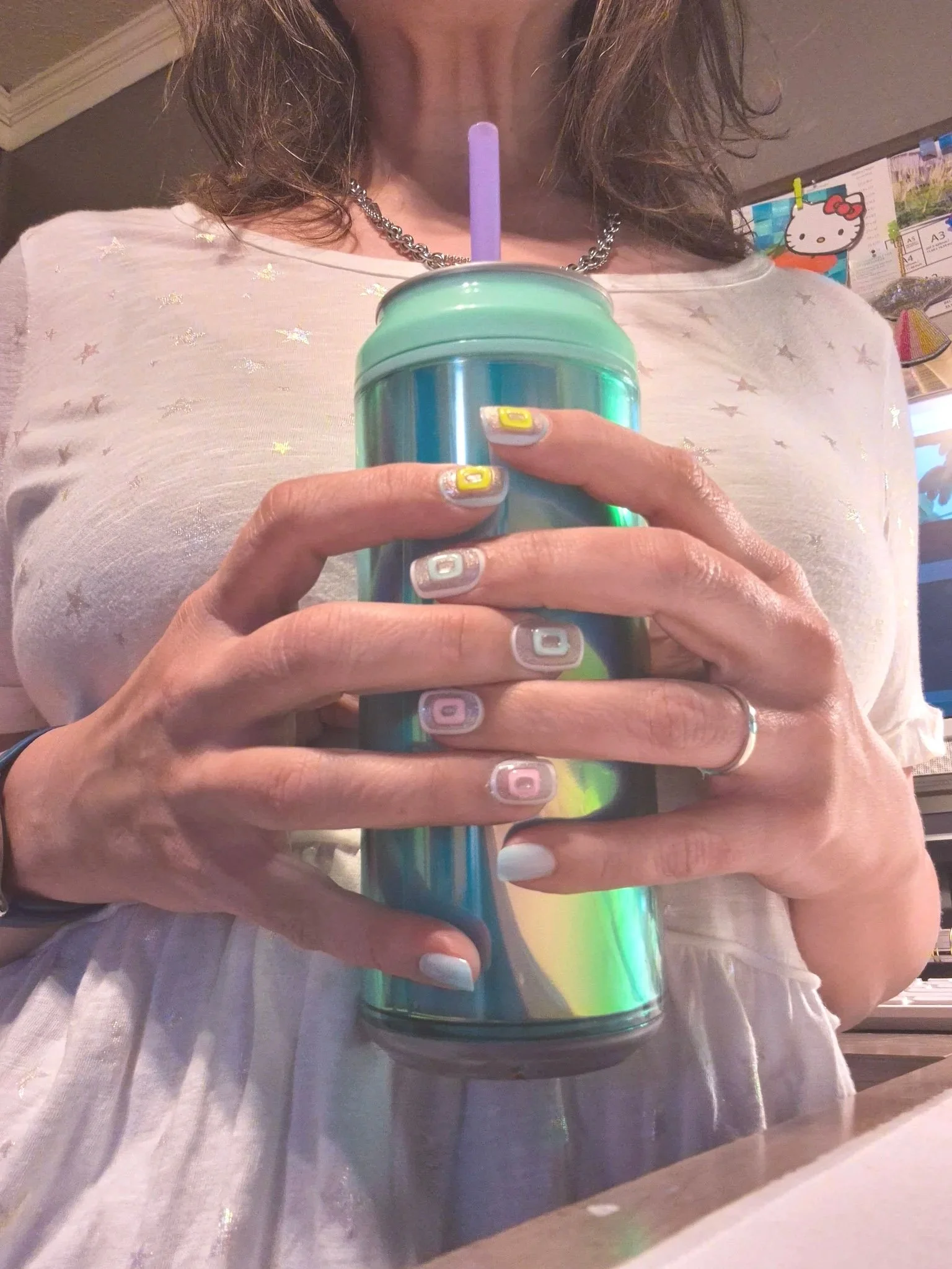 Hands holding an iridescent tumbler with colorful pastel nail art in a cozy studio space