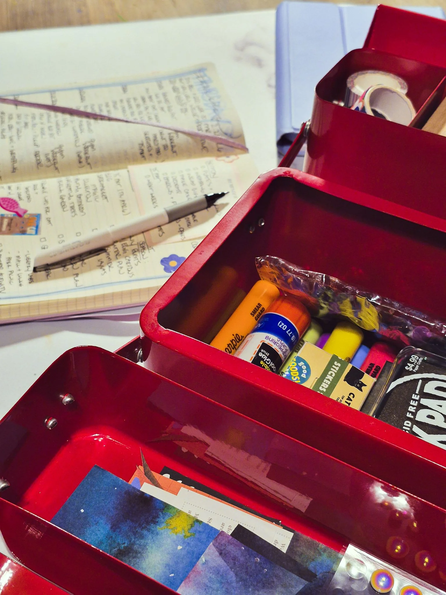 desk shot of a red toolbox filled with junk journal supplies journal open in background
