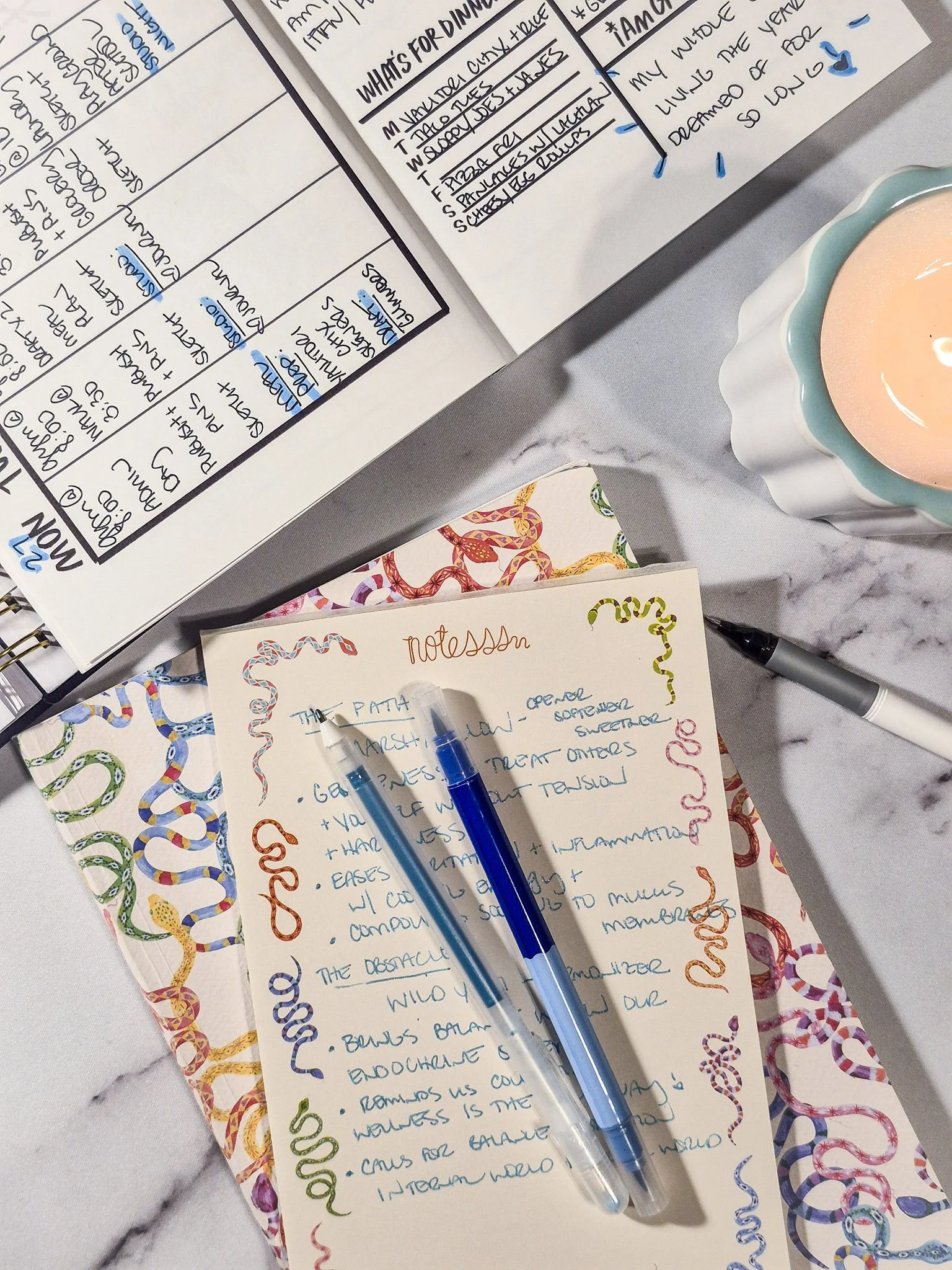 Handwritten notes on a decorative patterned notepad with colorful illustrated border and blue pens on top