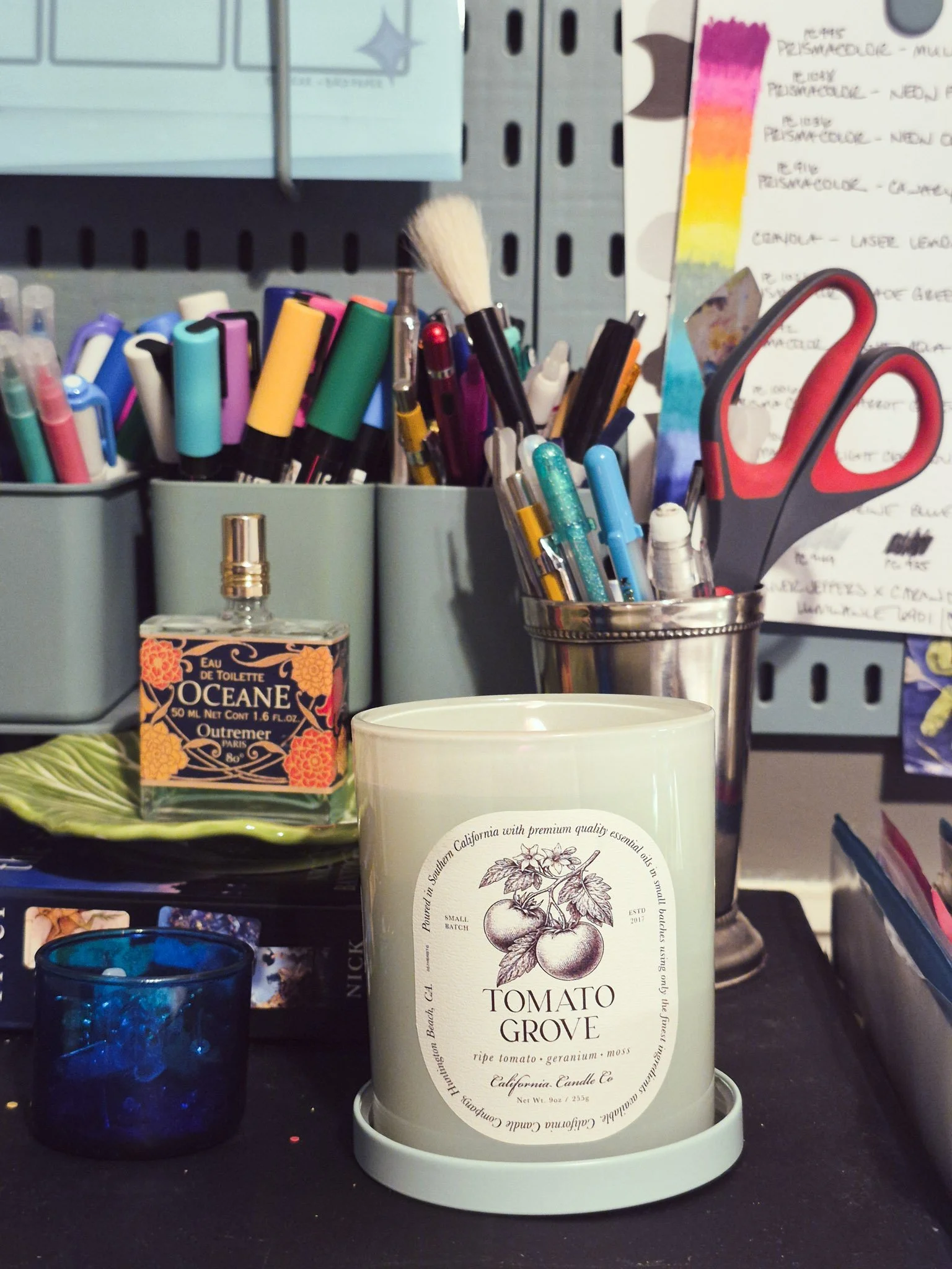 Cozy artist workspace with a tomato-scented candle, pens, and creative tools on a desk