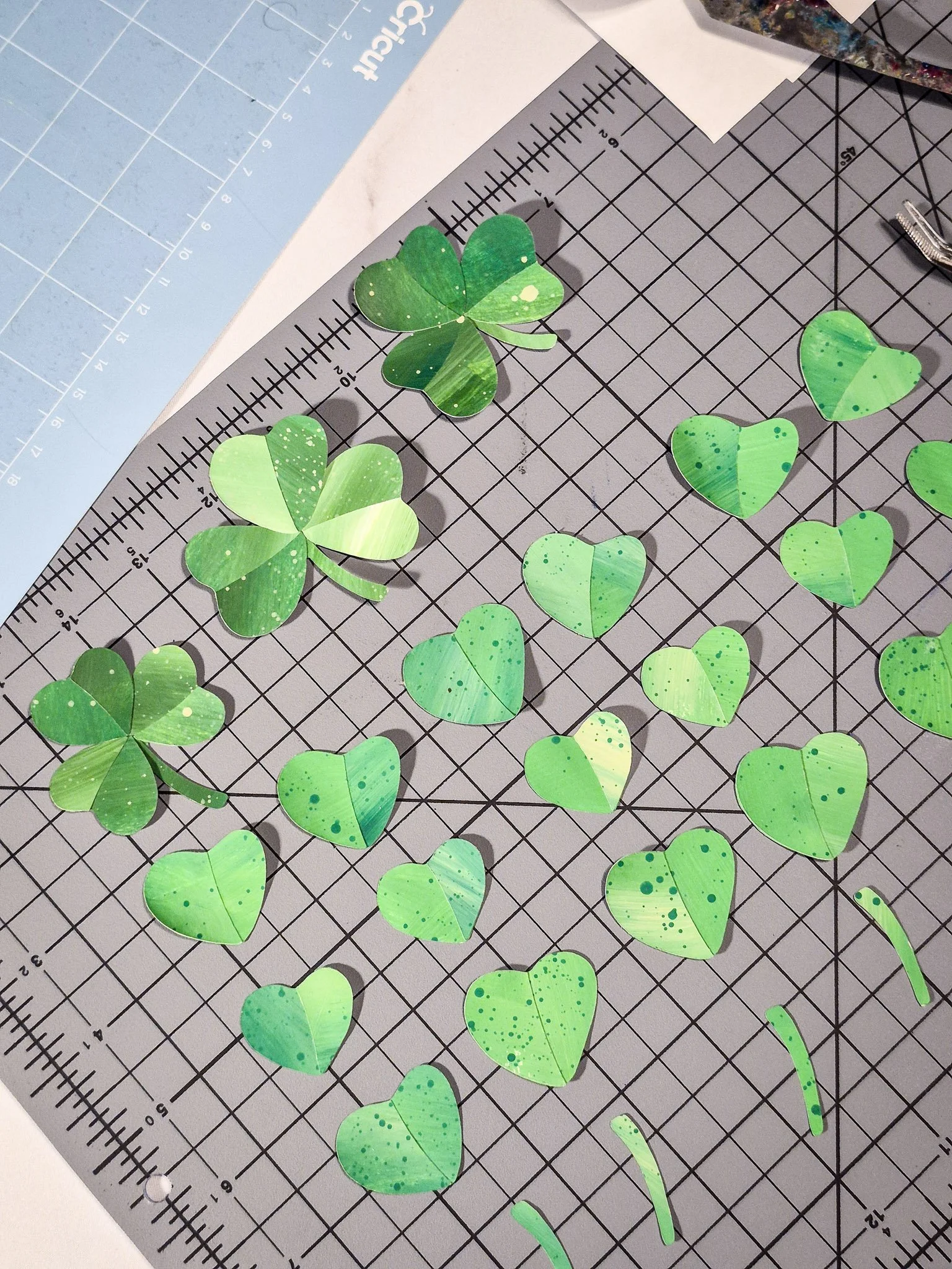 Cut paper clover pieces arranged on a grid cutting mat to plan a handmade repeat pattern layout